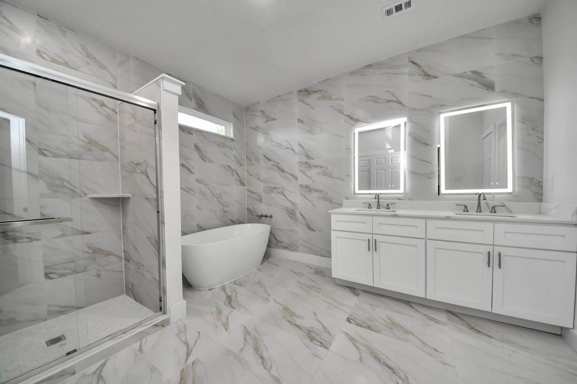 Luxurious bathroom featuring elegant marble tile, a spacious glass-enclosed shower, and a sleek freestanding bathtub, complemented by dual vanities with illuminated mirrors.