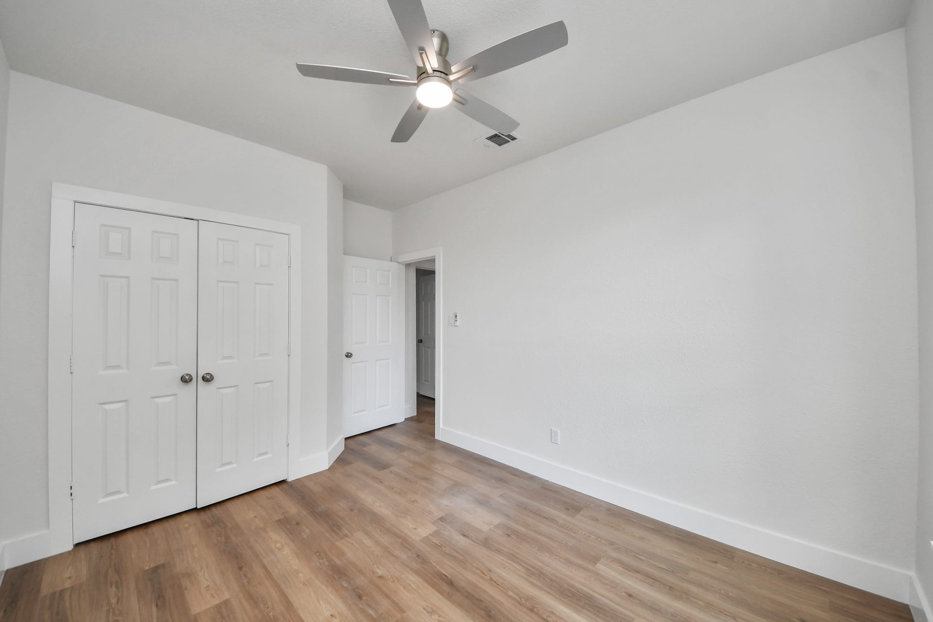 Bright and airy bedroom featuring a modern ceiling fan, spacious closet, and beautiful wood flooring.