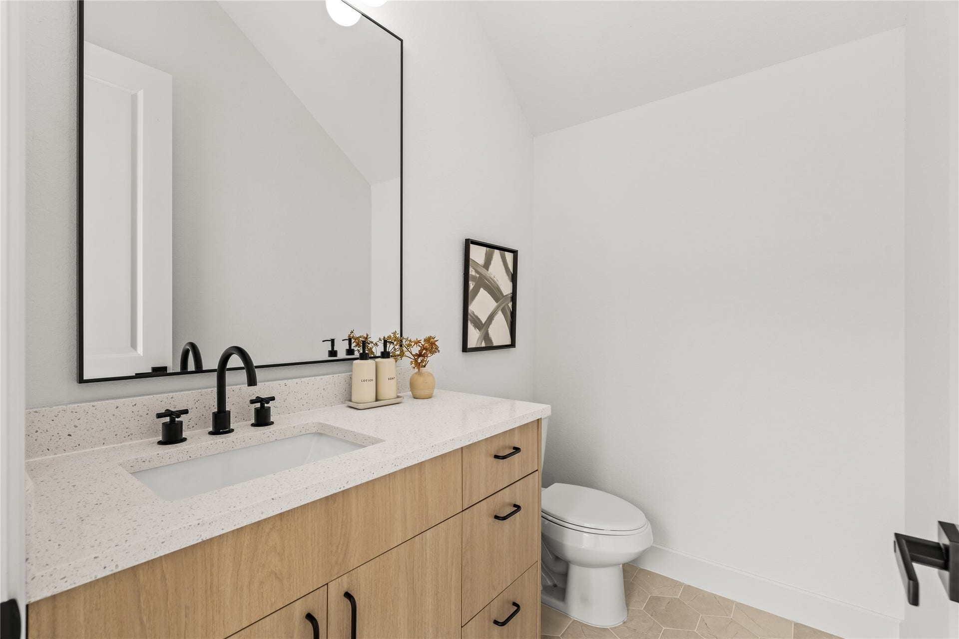 3012 & 3014 Beulah St, Houston, TX 77004 The main-floor powder room features a warm wood vanity with a white quartz countertop, an under-mount sink, and matte black hardware. A black gooseneck faucet pairs with a matching black-framed mirror, set against neutral vertical walls and geometric floor tiles.