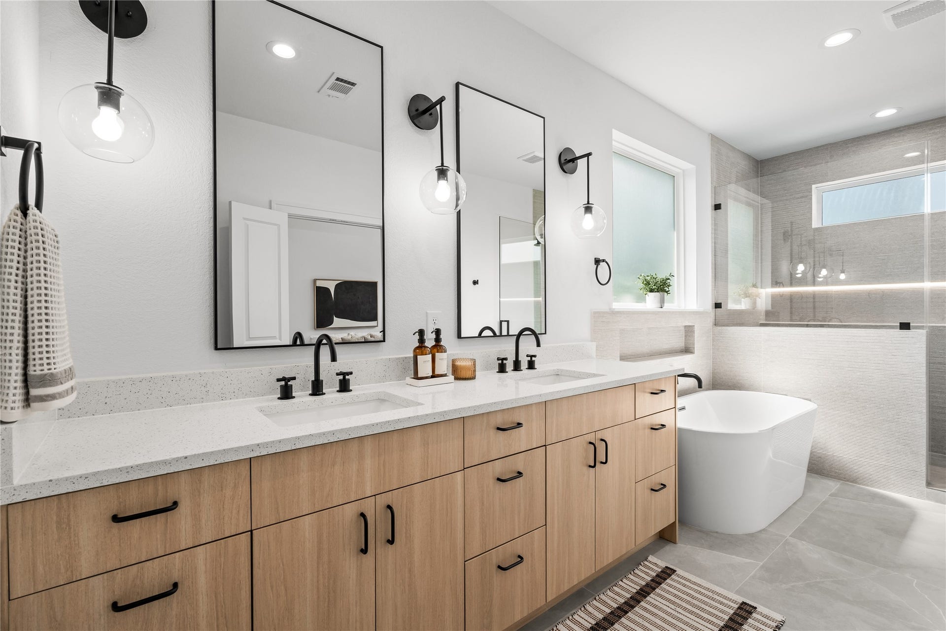 3012 & 3014 Beulah St, Houston, TX 77004 This view shows the large primary vanity with its double-sink layout and white quartz countertop. Warm wood cabinets with black hardware provide plenty of storage, while two large black-framed mirrors and glass globe sconces create a bright, functional space.