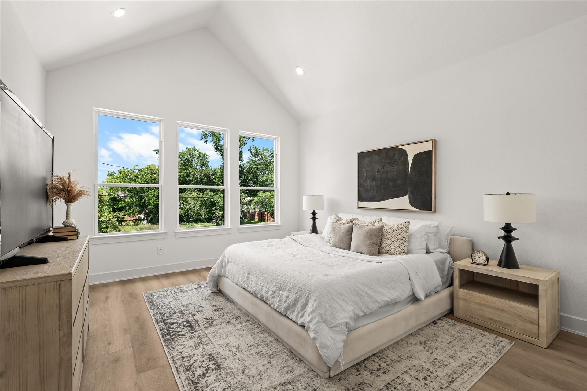 3012 & 3014 Beulah St, Houston, TX 77004 The primary bedroom features a dramatic vaulted ceiling and three large vertical windows that look out onto mature trees. The spacious layout easily fits a king-sized bed, matching nightstands, and a large dresser with room to spare.