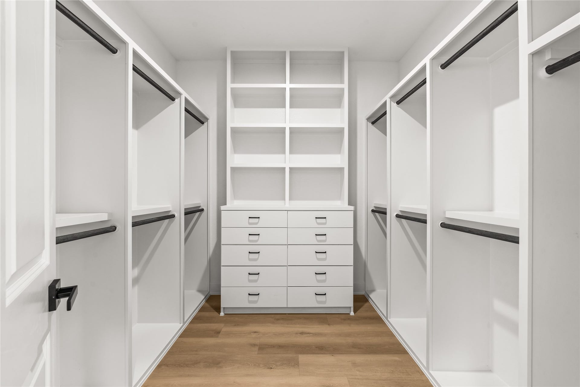 3012 & 3014 Beulah St, Houston, TX 77004 The massive primary walk-in closet features a white custom storage system. A central built-in dresser offers ten drawers with display shelving above, flanked by multiple wardrobe sections equipped with sturdy black hanging rods.