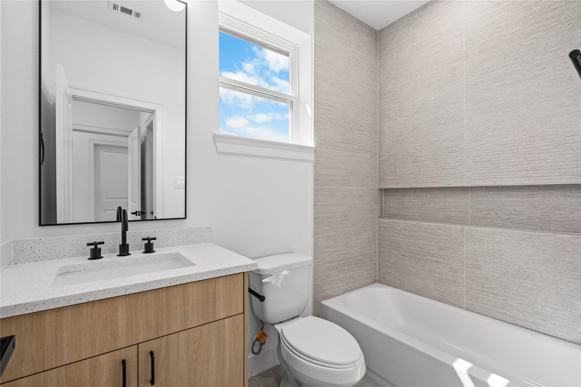 3012 & 3014 Beulah St, Houston, TX 77004 The third full bathroom features a warm wood vanity, a white quartz countertop, and a shower-tub combination. A large vertical window brings in excellent natural light, complemented by a durable, textured tile surround.