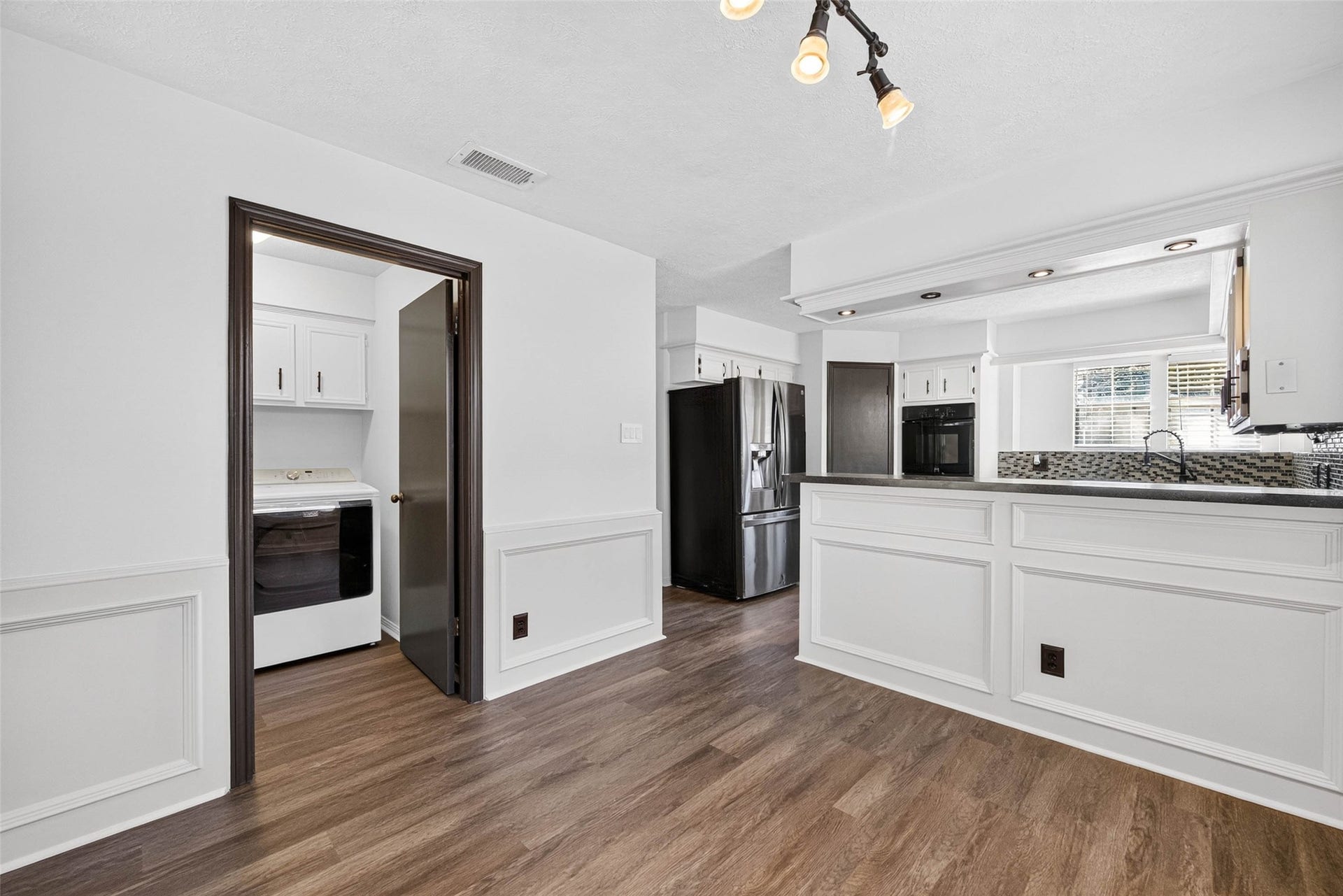 1123 Woodhorn Drive, Houston, TX 77062 View from the dining area toward the kitchen peninsula, with a stainless refrigerator, black double oven, and a doorway opening to the laundry room.