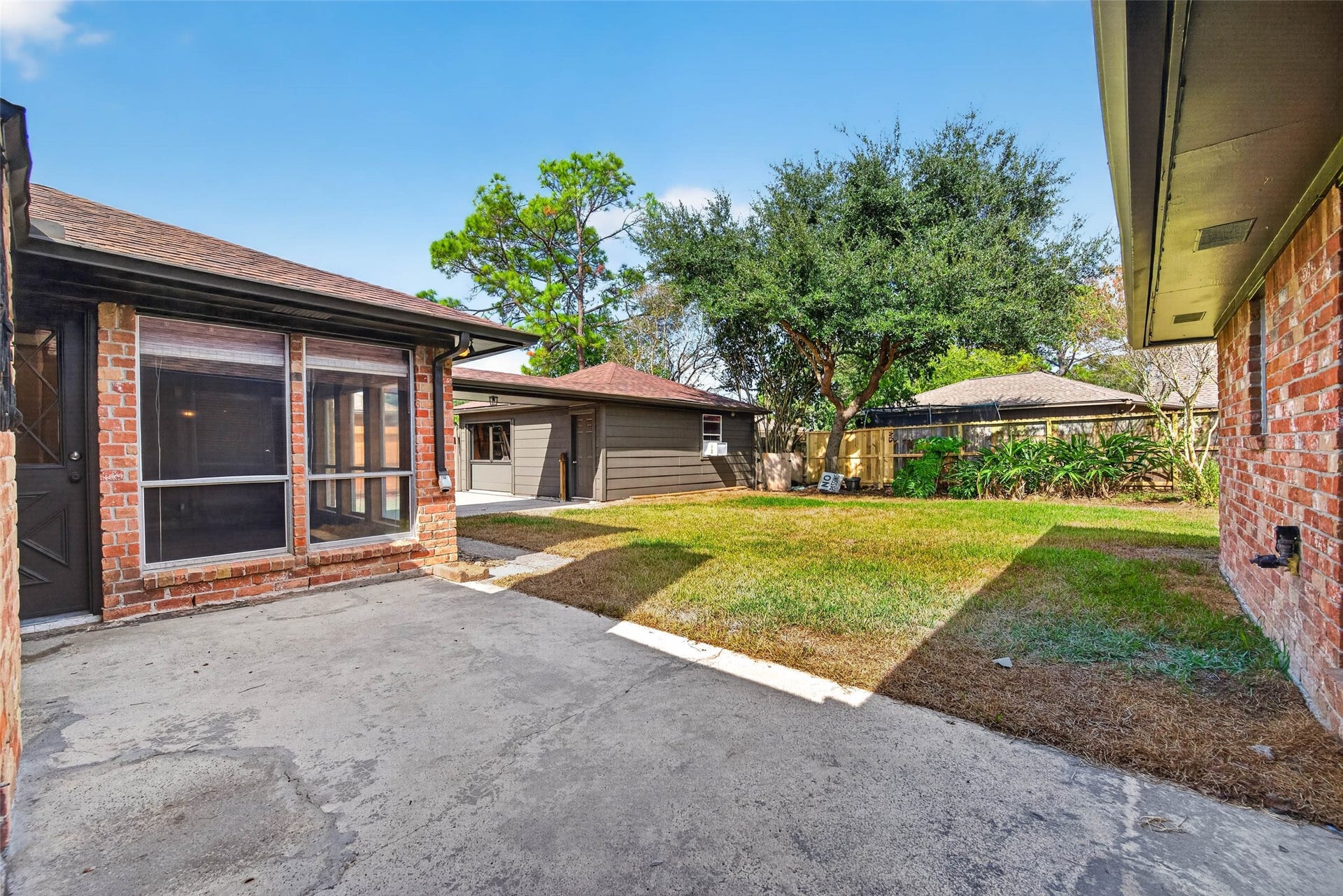 1123 Woodhorn Drive, Houston, TX 77062 Backyard view with the brick house wall, large windows, lawn, mature trees, and wooden fencing.