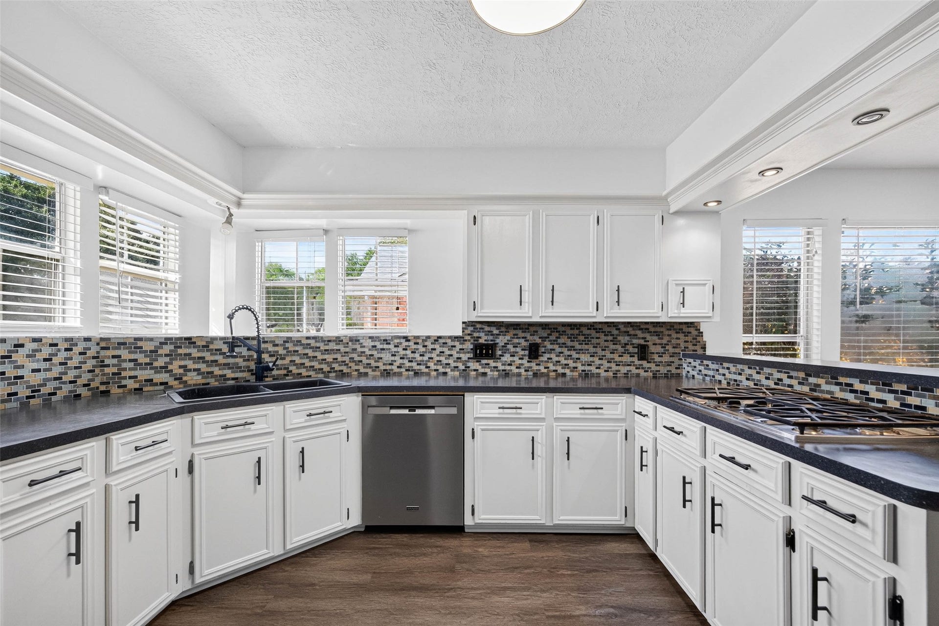 1123 Woodhorn Drive, Houston, TX 77062 Straight-on kitchen view with cabinets, mosaic tile backsplash, double sink beneath windows, stainless dishwasher, and gas cooktop on the side peninsula.