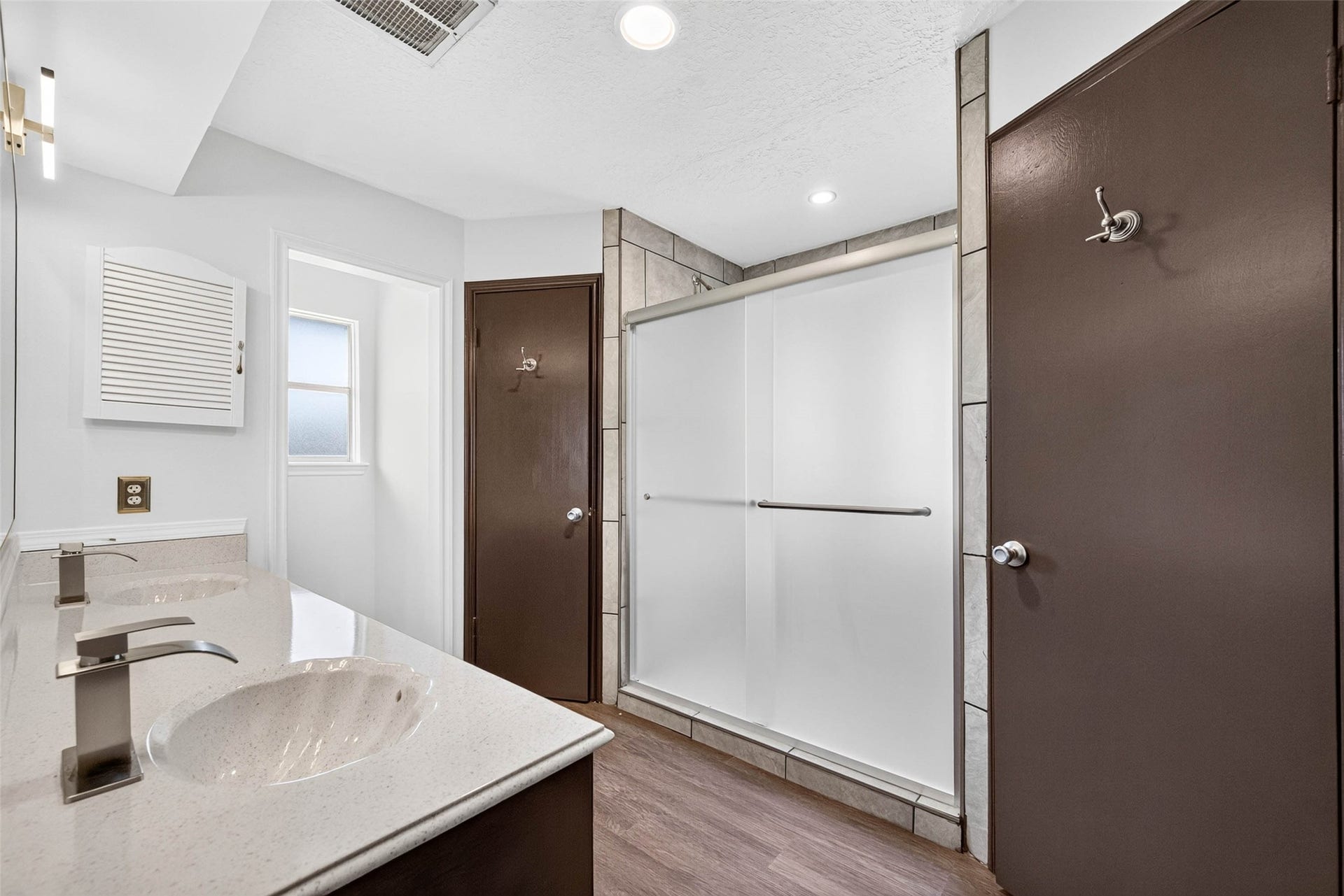 1123 Woodhorn Drive, Houston, TX 77062 En-suite bathroom with a double vanity in dark wood, a speckled countertop, a frosted glass shower enclosure with tile surround, and wood-look flooring.