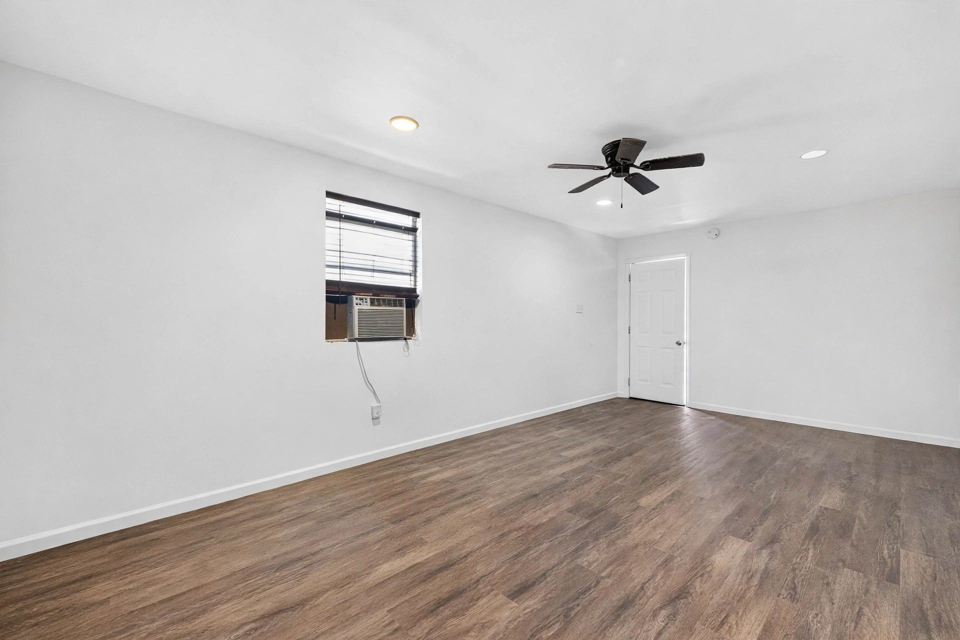 1123 Woodhorn Drive, Houston, TX 77062 Another angle of the flexible interior room, with wood-look flooring, a dark ceiling fan, recessed lights, and a window air-conditioning unit.