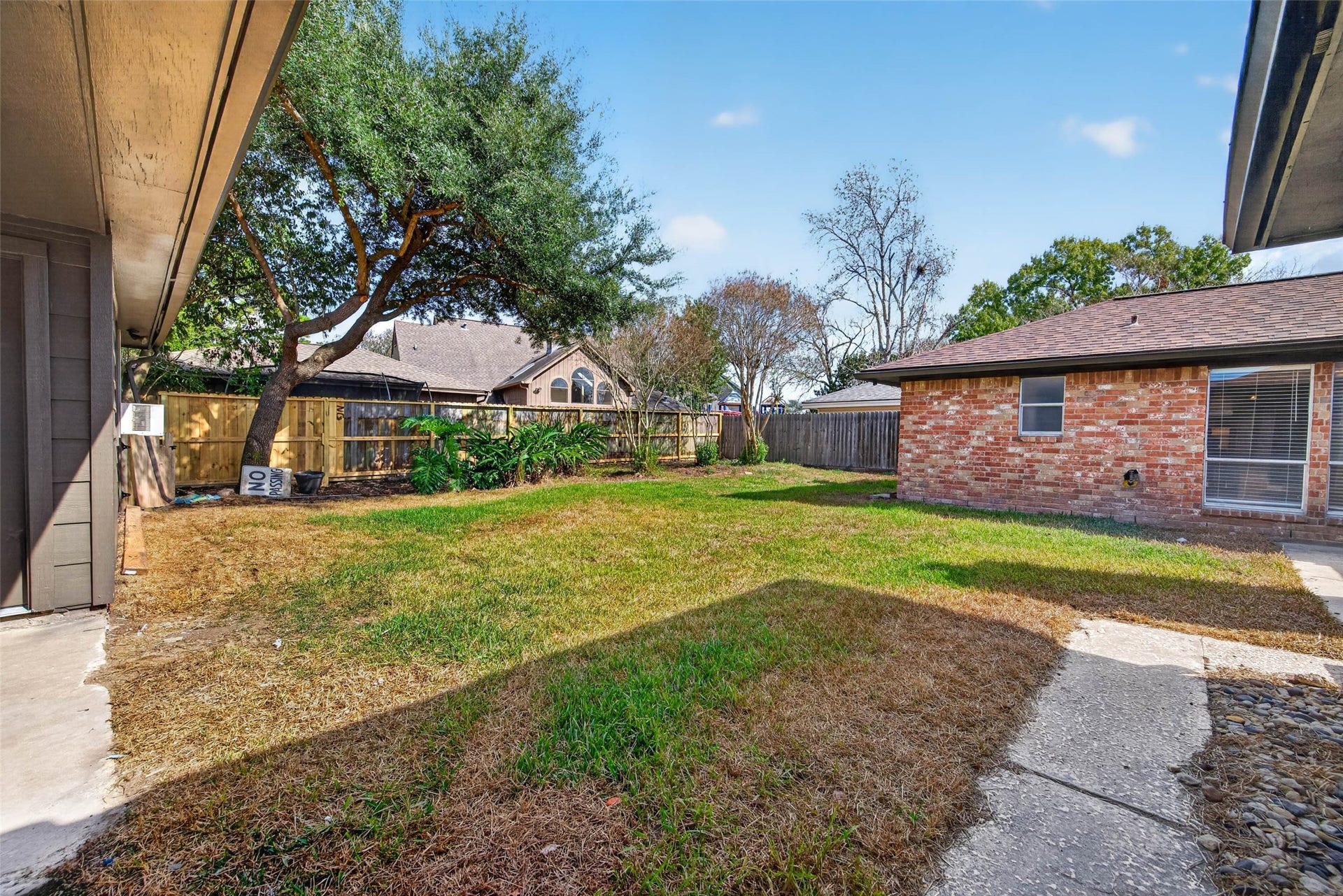 1123 Woodhorn Drive, Houston, TX 77062 Wide backyard view across the lawn to the brick rear of the home, with a mature shade tree, wooden fencing, and a concrete walk.