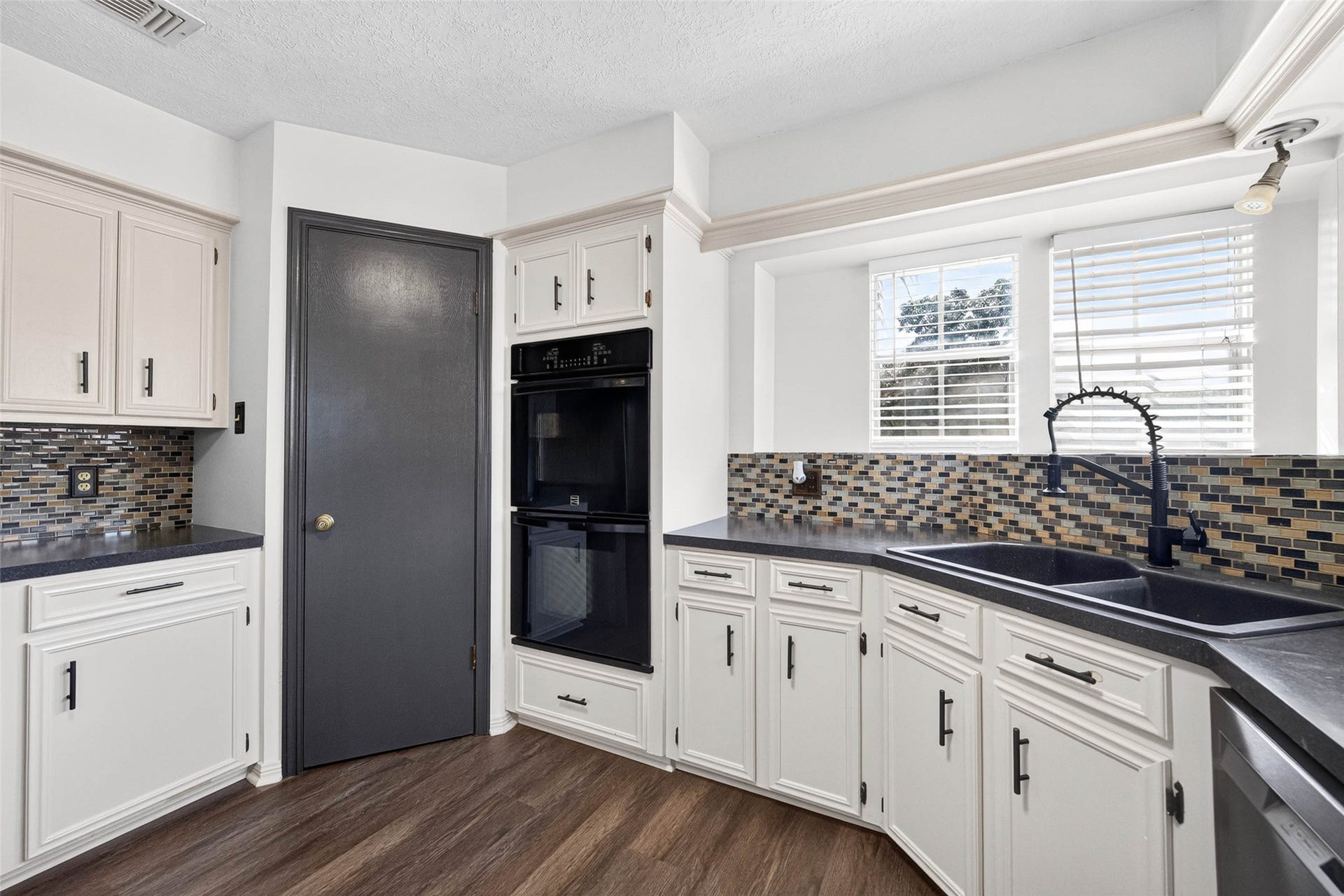 1123 Woodhorn Drive, Houston, TX 77062 Kitchen view centered on the dark double-basin sink with a gooseneck faucet, set beneath windows with blinds and flanked by cabinets and the black double oven.