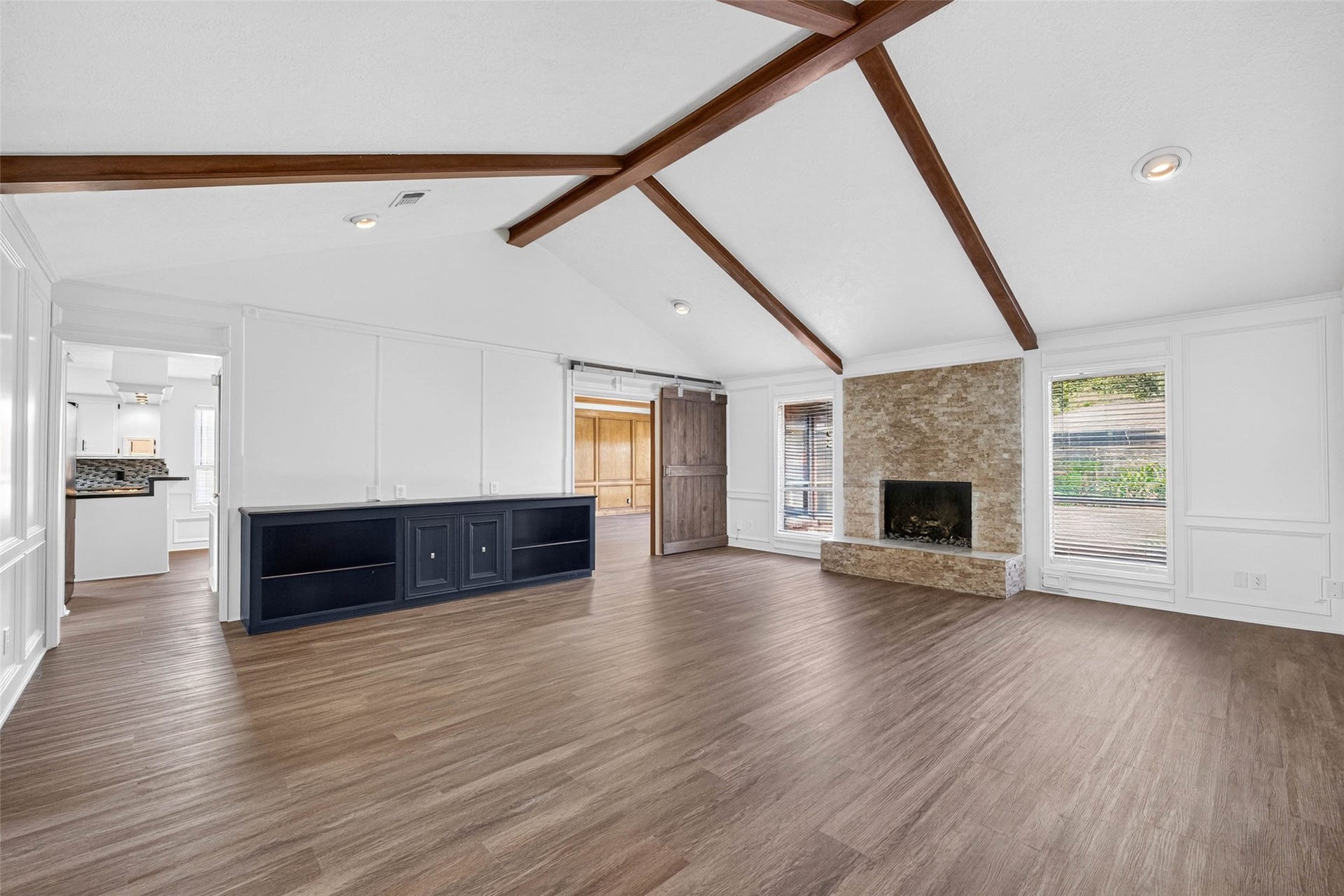 1123 Woodhorn Drive, Houston, TX 77062 Living room under a vaulted ceiling with crossing dark wood beams, a stacked-stone fireplace, paneled walls, and a dark wood sliding barn door opening to the paneled room.