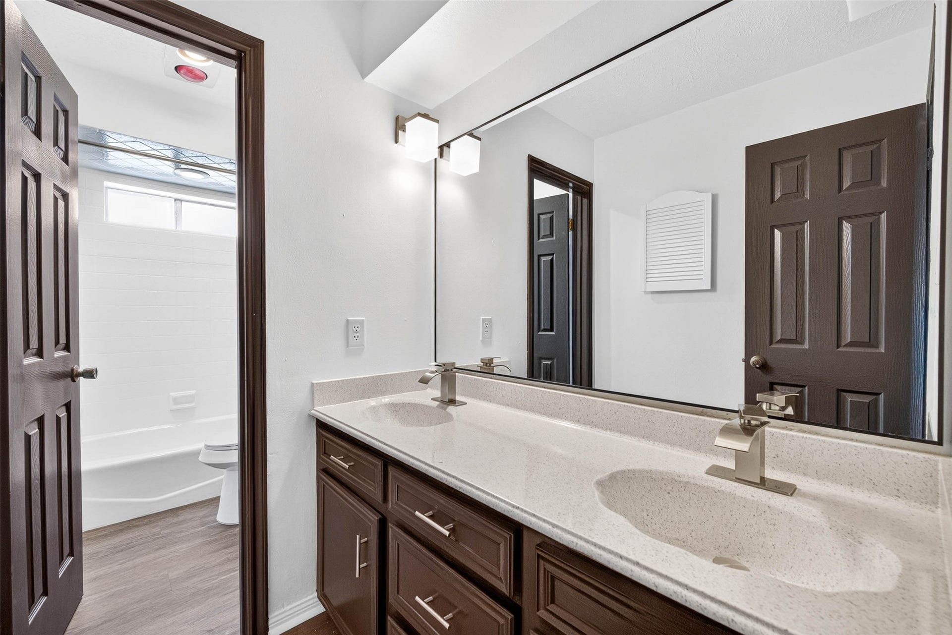 1123 Woodhorn Drive, Houston, TX 77062 Bathroom with a long double vanity in dark wood, a speckled countertop, and a large mirror, with the tub and toilet room opening to the left.