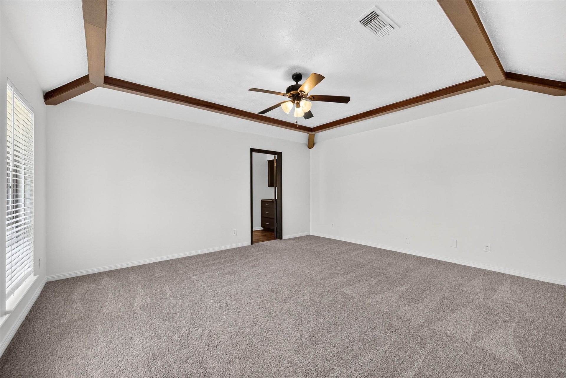 1123 Woodhorn Drive, Houston, TX 77062 Large carpeted bedroom under a vaulted ceiling with dark wood beams and trim, a ceiling fan with lights, and a doorway to the en-suite bath.