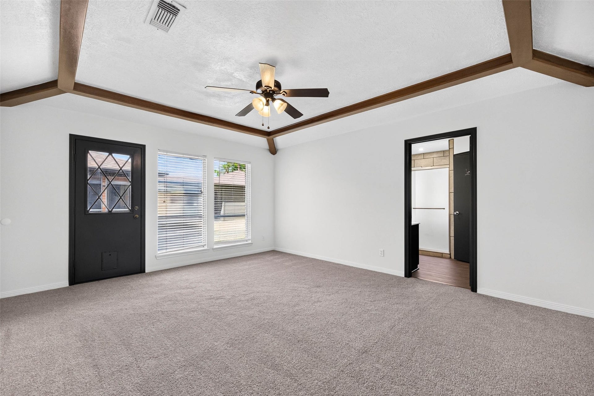 1123 Woodhorn Drive, Houston, TX 77062 Another angle of the large beamed bedroom, with a black glass-paneled door, two windows with blinds, and the en-suite bath doorway.
