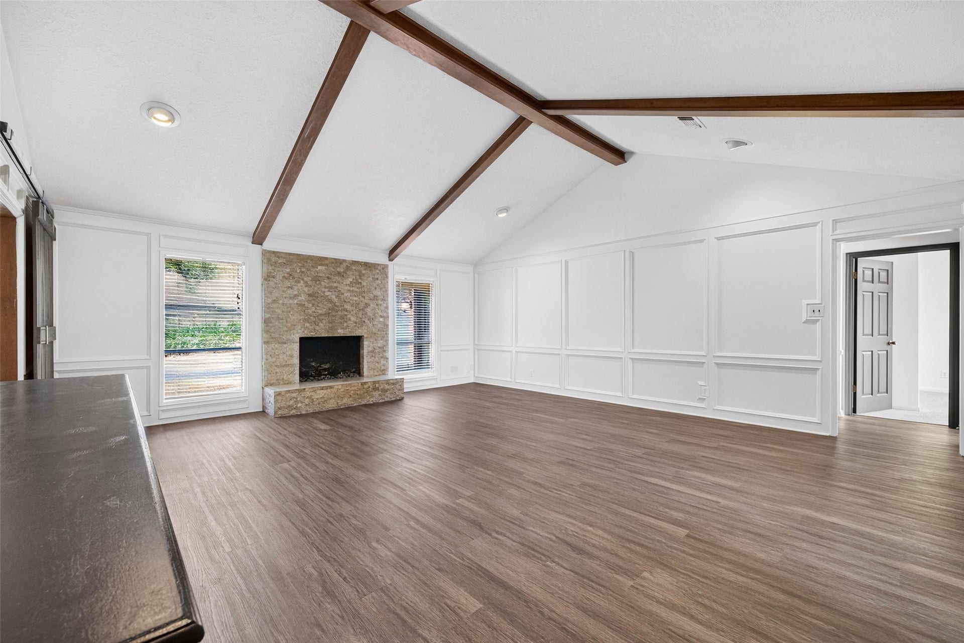 1123 Woodhorn Drive, Houston, TX 77062 Living room angle toward the stacked-stone fireplace with raised hearth, flanked by windows with blinds, under crossing wood beams.