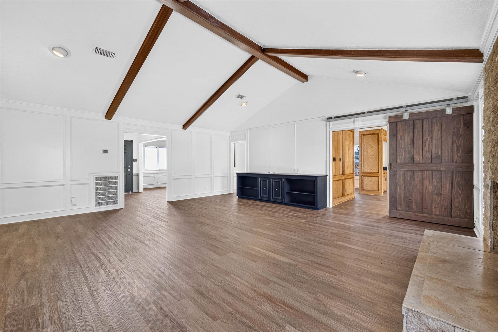 1123 Woodhorn Drive, Houston, TX 77062 Living room angle centered on the dark wood sliding barn door, with crossing beams, paneled walls, and the stone fireplace hearth at the edge.