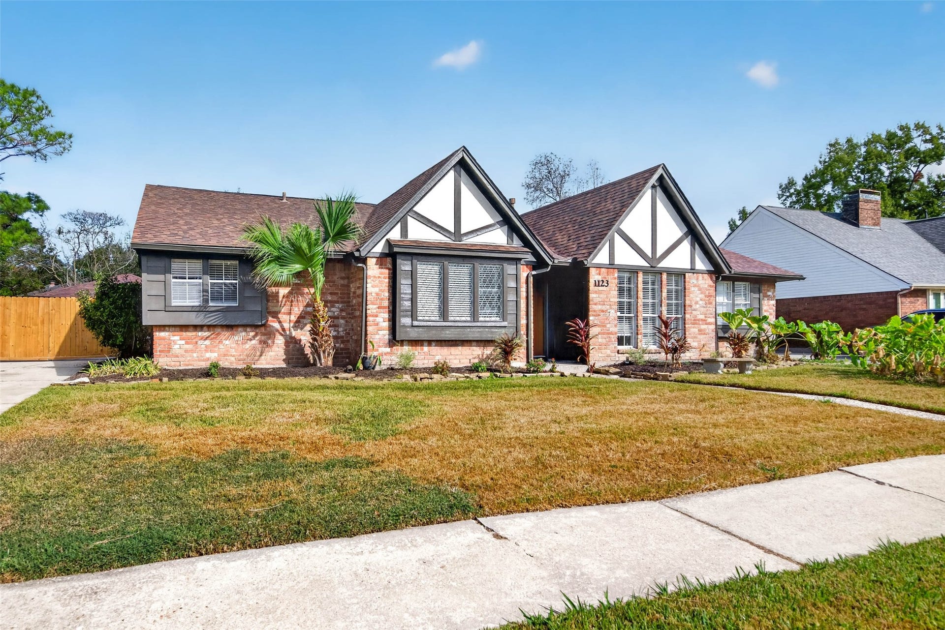 1123 Woodhorn Drive, Houston, TX 77062 Front view from the sidewalk across the lawn, with the white gables and dark timber trim, bay window, palm, and wooden fence at the side.