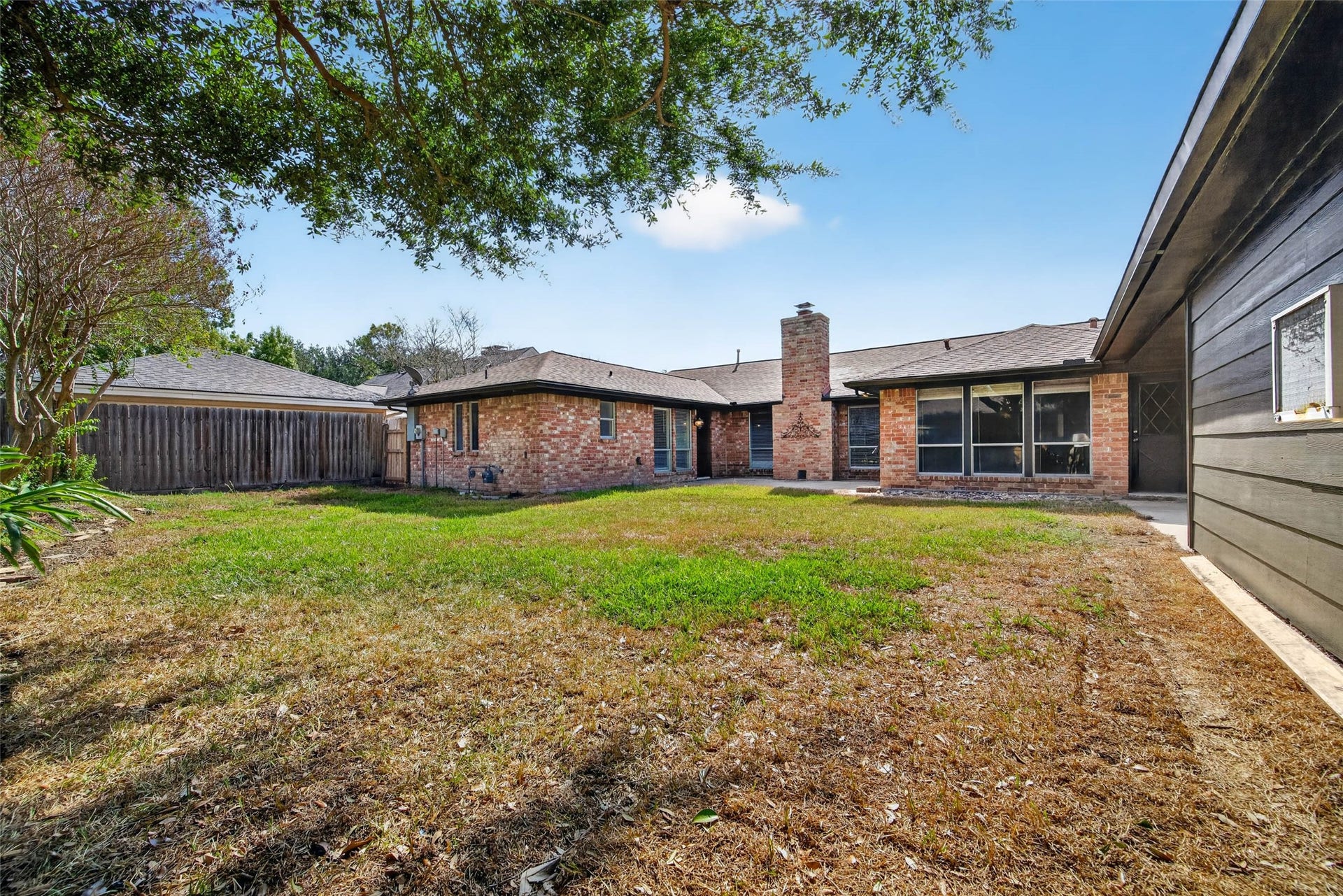 1123 Woodhorn Drive, Houston, TX 77062 Wide backyard view of the brick rear of the home with its chimney and large windows, framed by lawn, fencing, and mature trees.