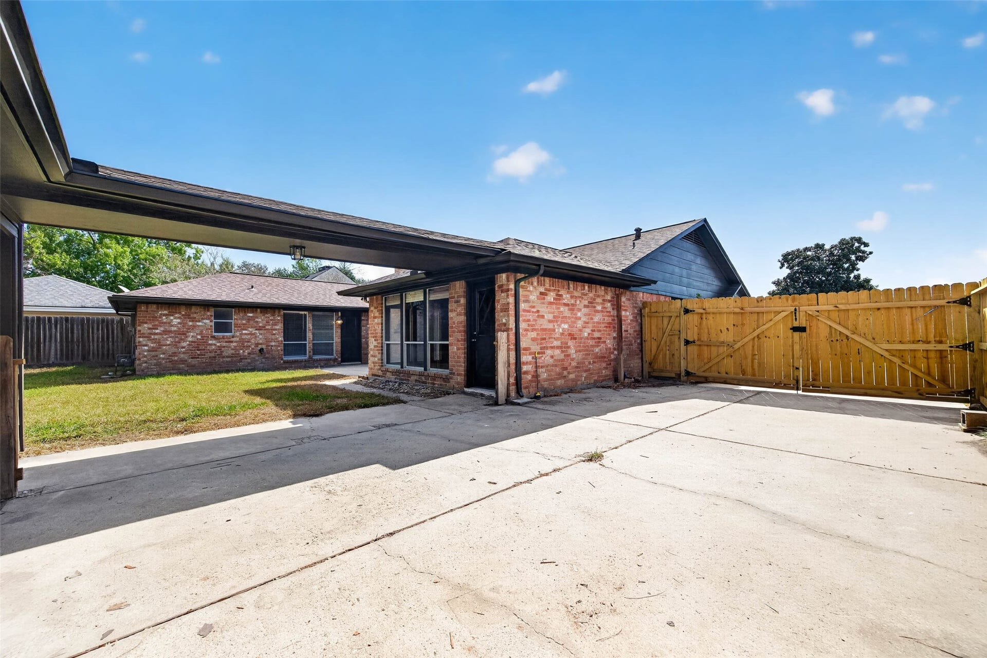 1123 Woodhorn Drive, Houston, TX 77062 Covered area and concrete driveway beside the brick house, with a wooden double gate opening to the lawn.