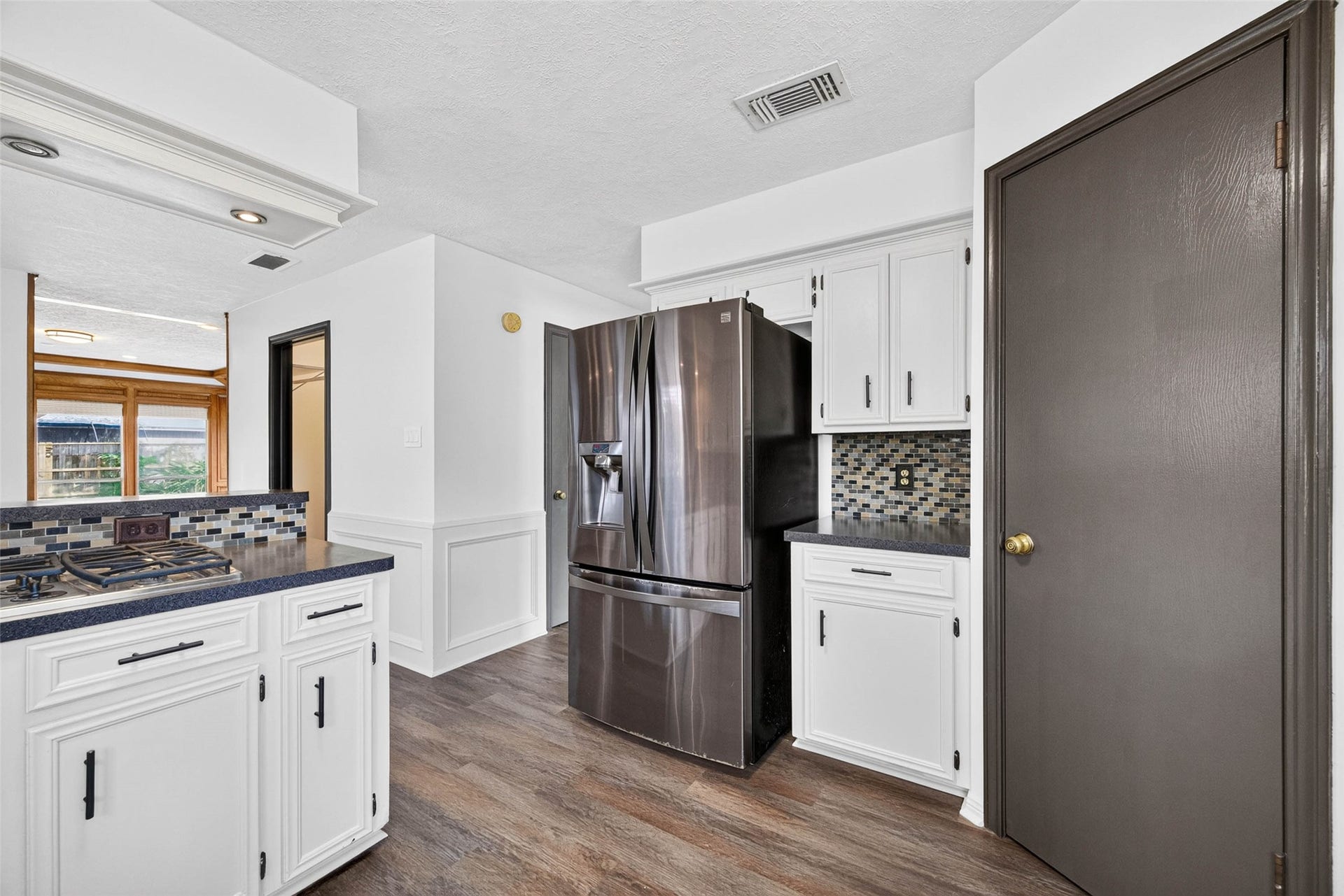 1123 Woodhorn Drive, Houston, TX 77062 Kitchen angle with a stainless French-door refrigerator, cabinets, mosaic tile backsplash, and a gas cooktop, with the paneled living room visible beyond.