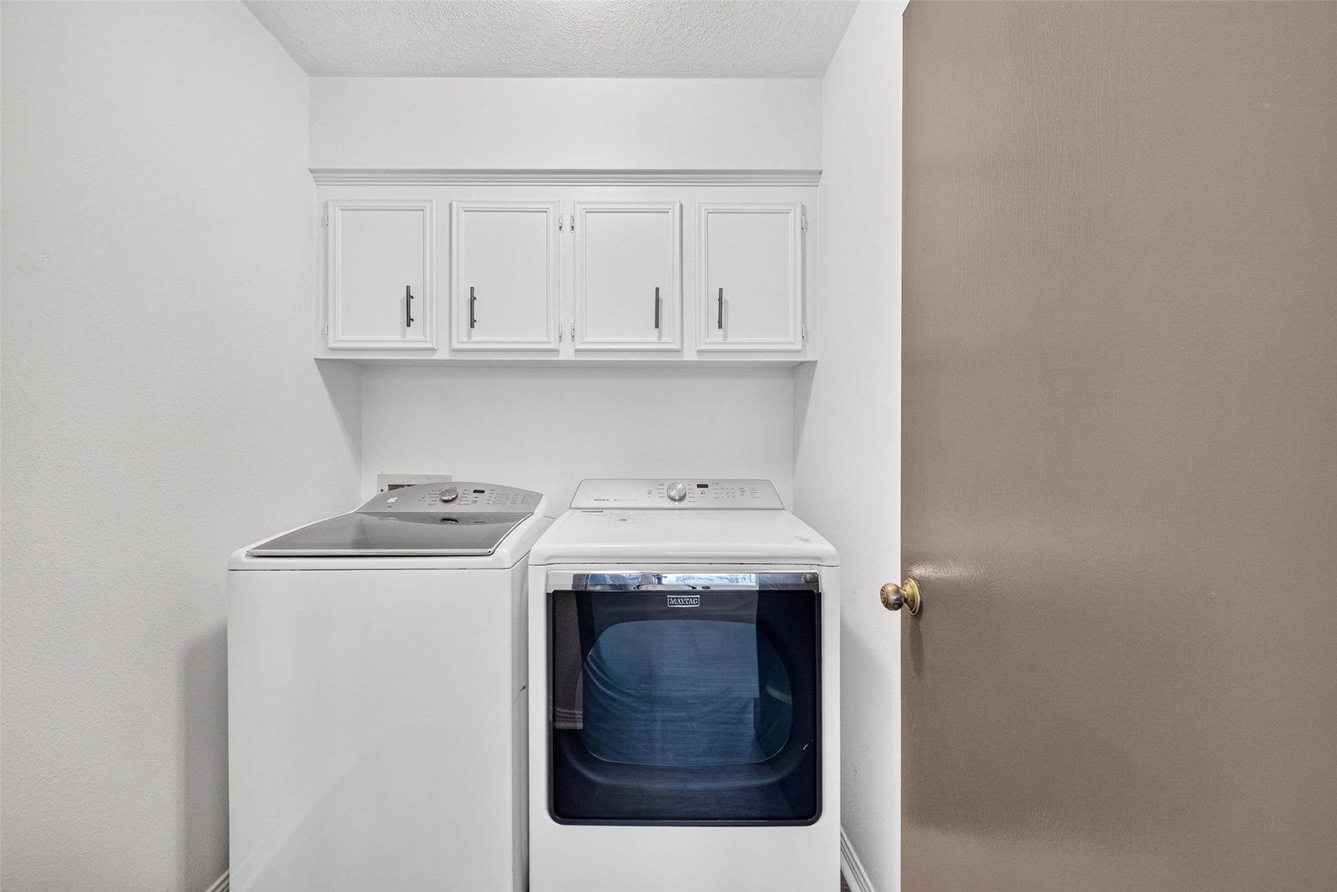 1123 Woodhorn Drive, Houston, TX 77062 Laundry room with a washer and dryer side by side and upper cabinets for storage.