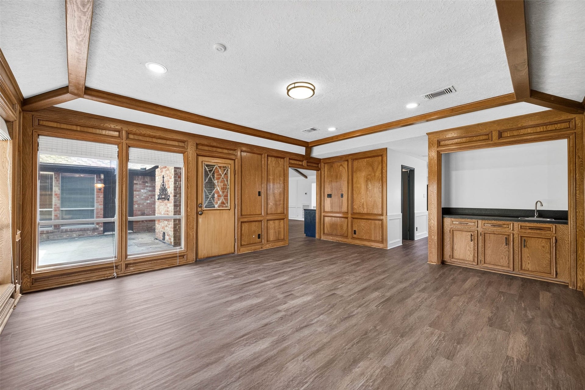 1123 Woodhorn Drive, Houston, TX 77062 Paneled living room view toward the bar, with glass-paneled wood doors, wide windows to the patio, and an open doorway to the kitchen.