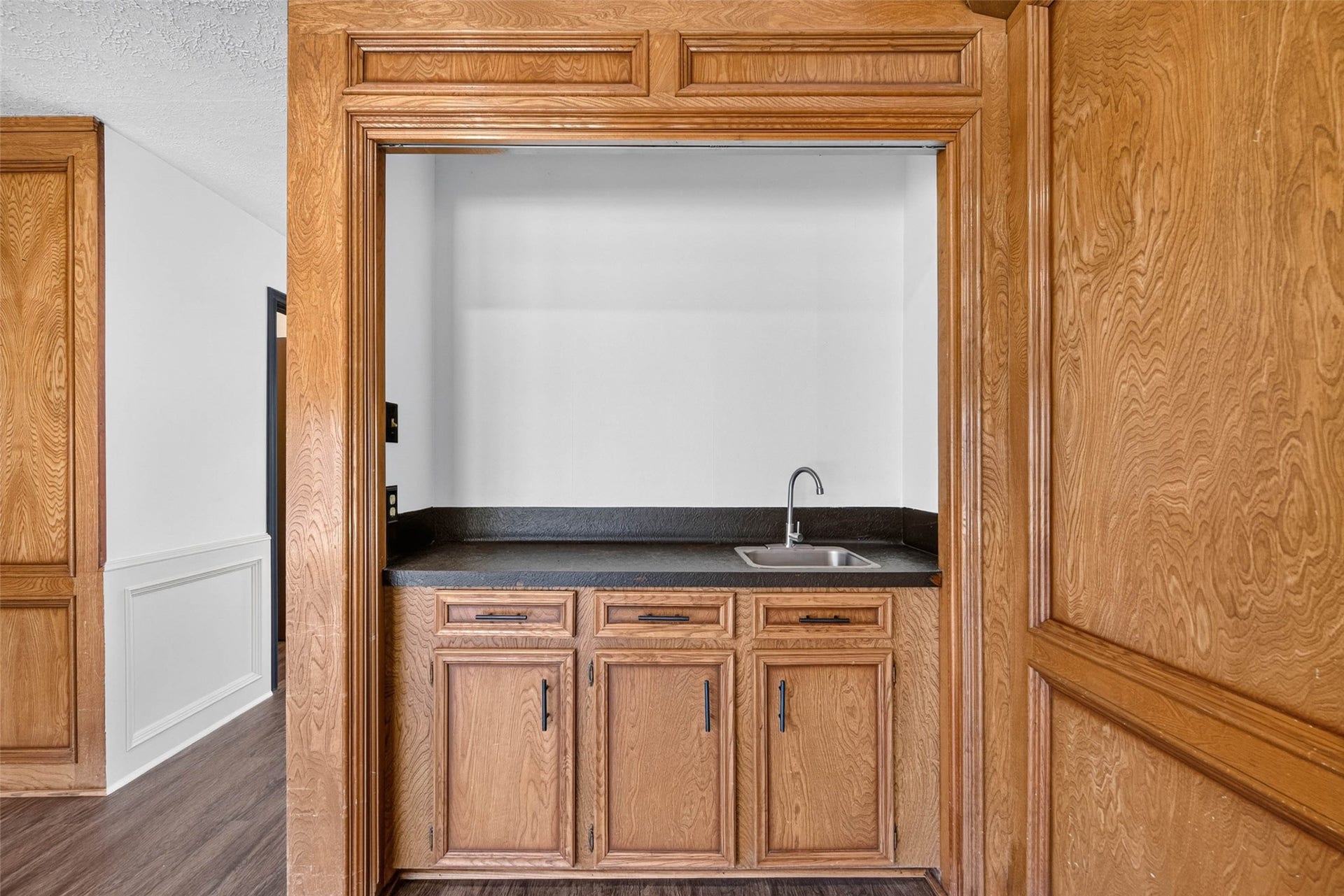 1123 Woodhorn Drive, Houston, TX 77062 Close-up of the built-in bar nook, with wood cabinets, a dark countertop, and a sink framed by the room's wood paneling.
