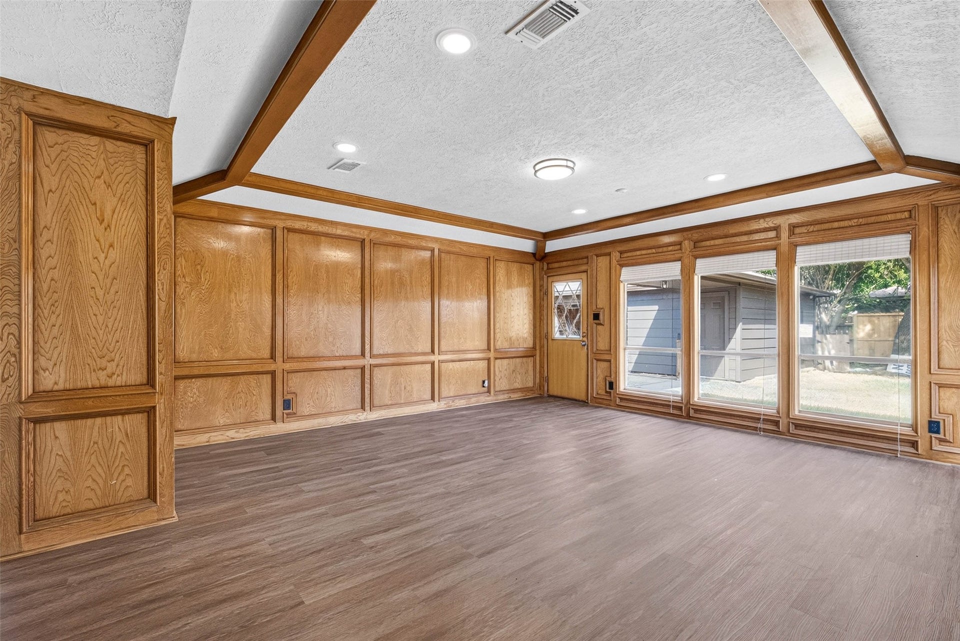 1123 Woodhorn Drive, Houston, TX 77062 Wood-paneled walls with raised panel detailing, exposed wood beams, and large windows overlooking the yard set the tone for this open living room on wood-look flooring.