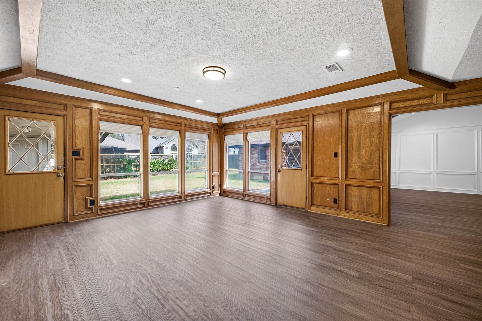 1123 Woodhorn Drive, Houston, TX 77062 Corner view of the paneled living room, where a full wall of windows frames the backyard and two glass-paneled wood doors open to the patio.