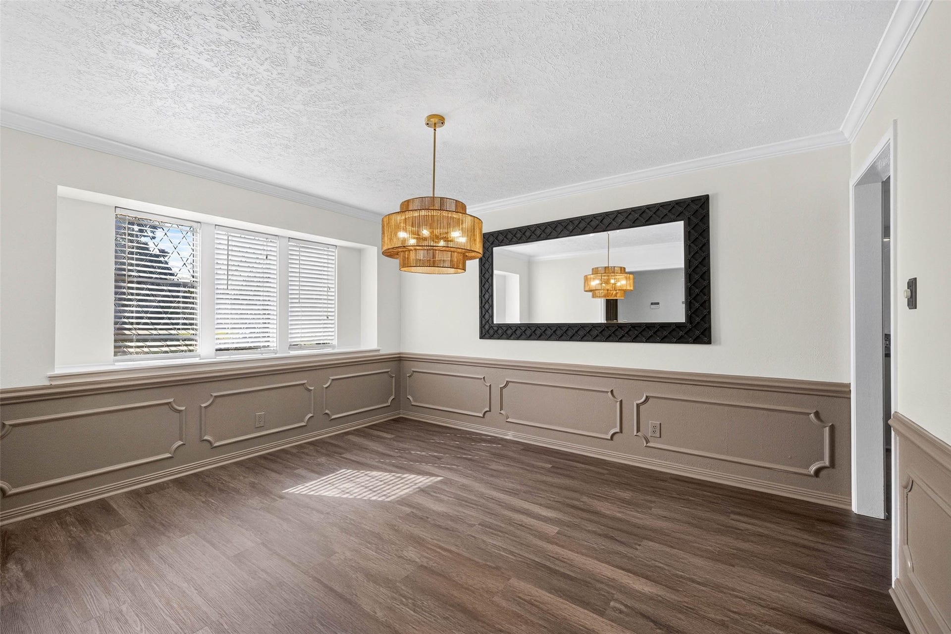 1123 Woodhorn Drive, Houston, TX 77062 Another angle of the front room, with wainscoted walls, three windows with blinds, a tiered pendant light, and a doorway to the next room.