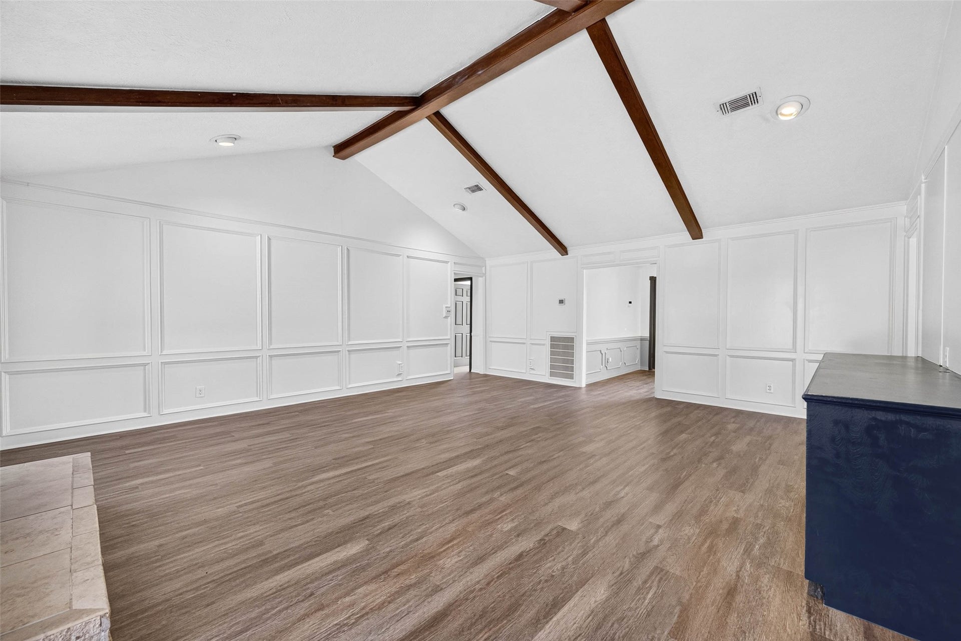 1123 Woodhorn Drive, Houston, TX 77062 Living room view across wood-look flooring to full-wall panel molding, crossing beams, and the stone hearth, with a doorway to the front room.