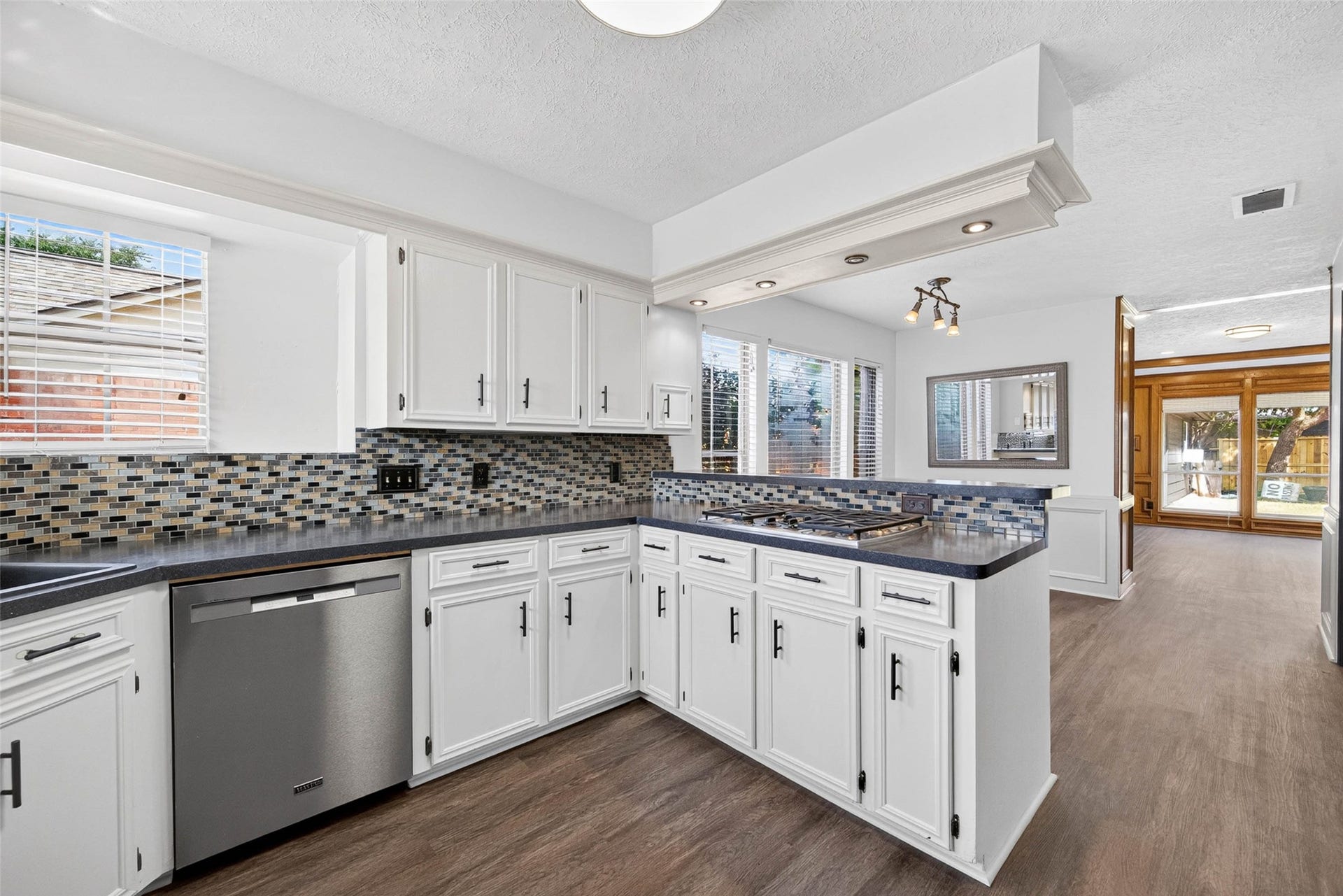 1123 Woodhorn Drive, Houston, TX 77062 Wide kitchen view along the cabinetry and mosaic backsplash, with the gas cooktop on the peninsula and the dining area and paneled room opening beyond.