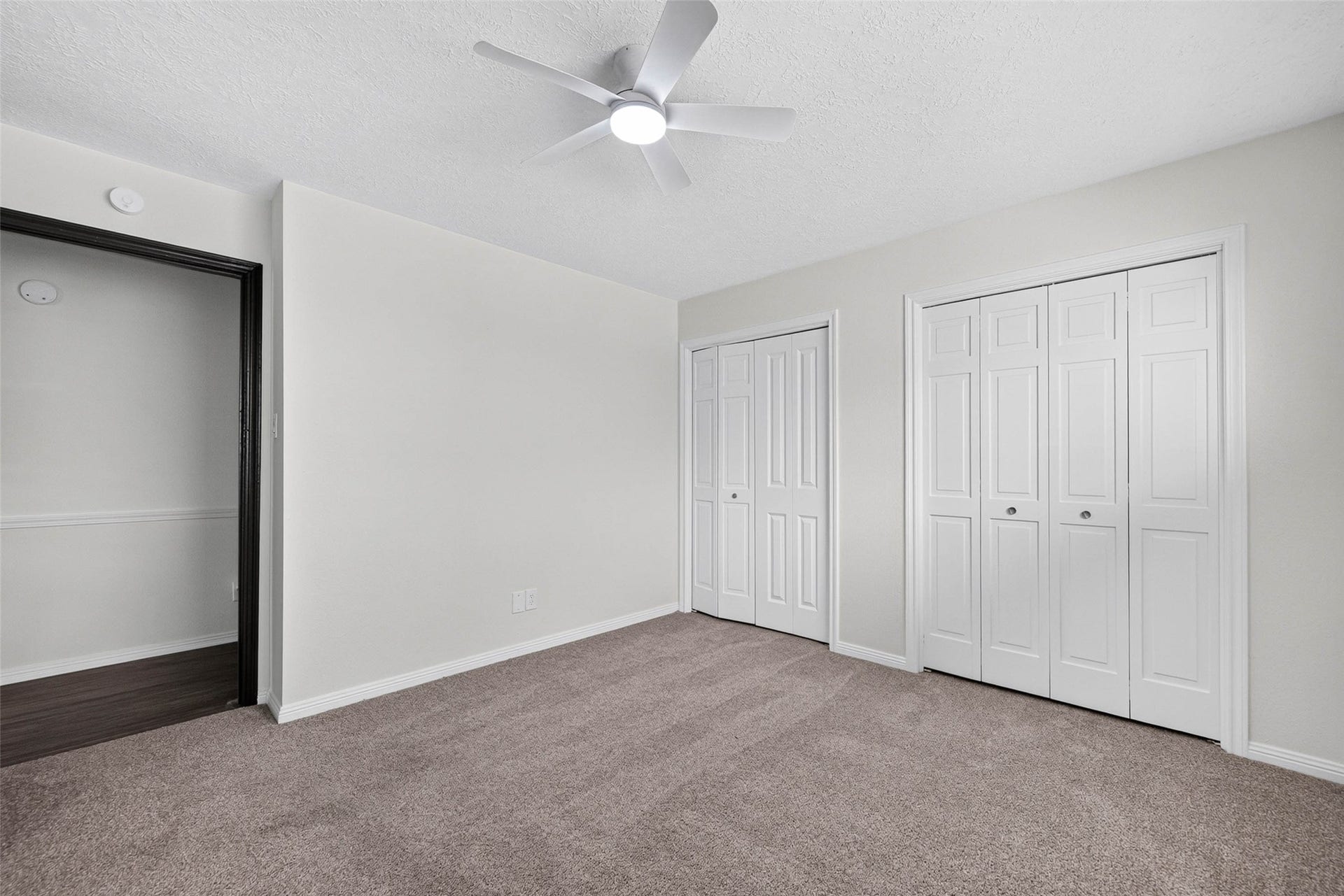 1123 Woodhorn Drive, Houston, TX 77062 Carpeted bedroom with two sets of closet doors, a ceiling fan with light, and a doorway opening to a wood-look floored room.