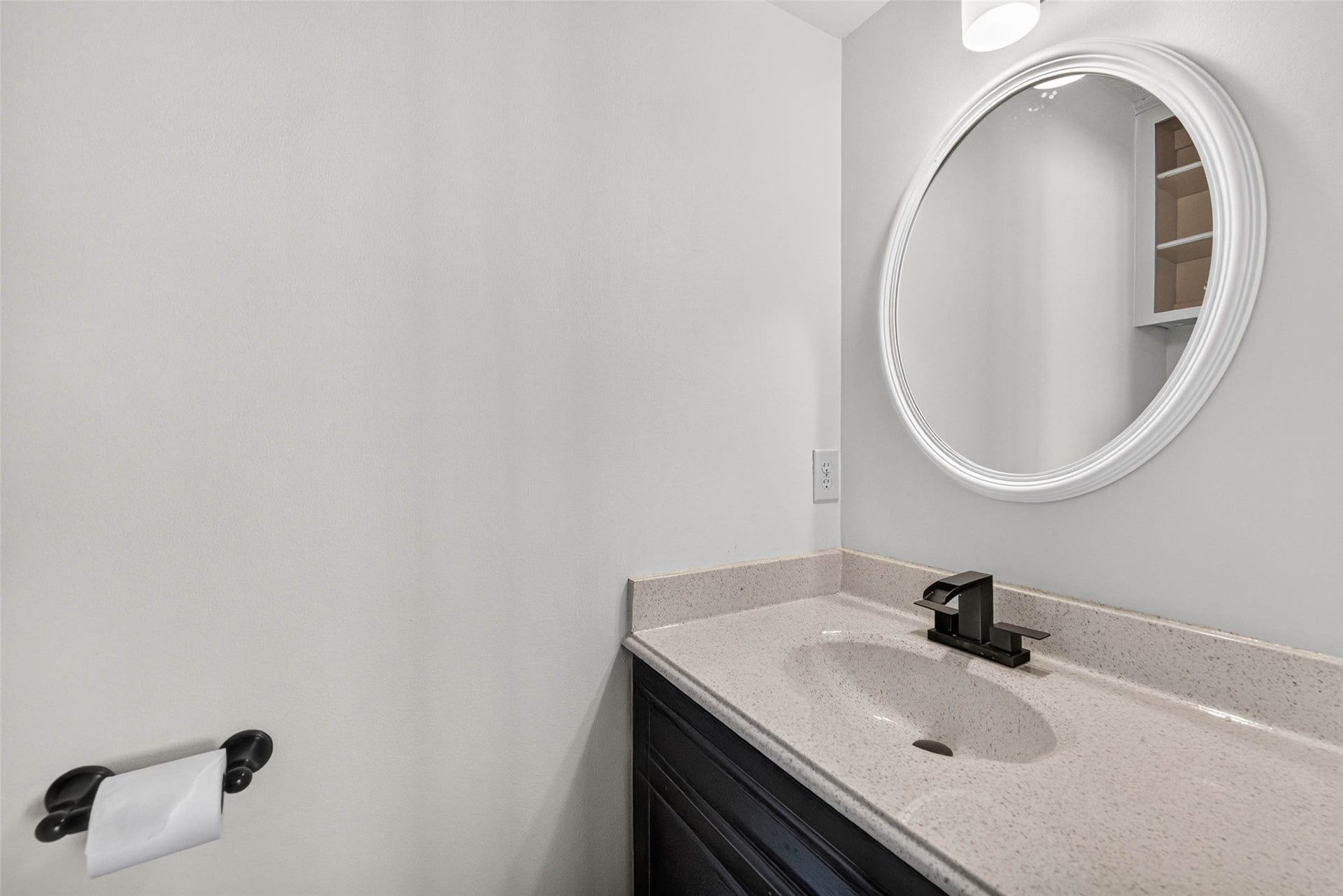 1123 Woodhorn Drive, Houston, TX 77062 Half bathroom with a single dark-wood vanity, speckled countertop, black faucet, and a large round mirror.