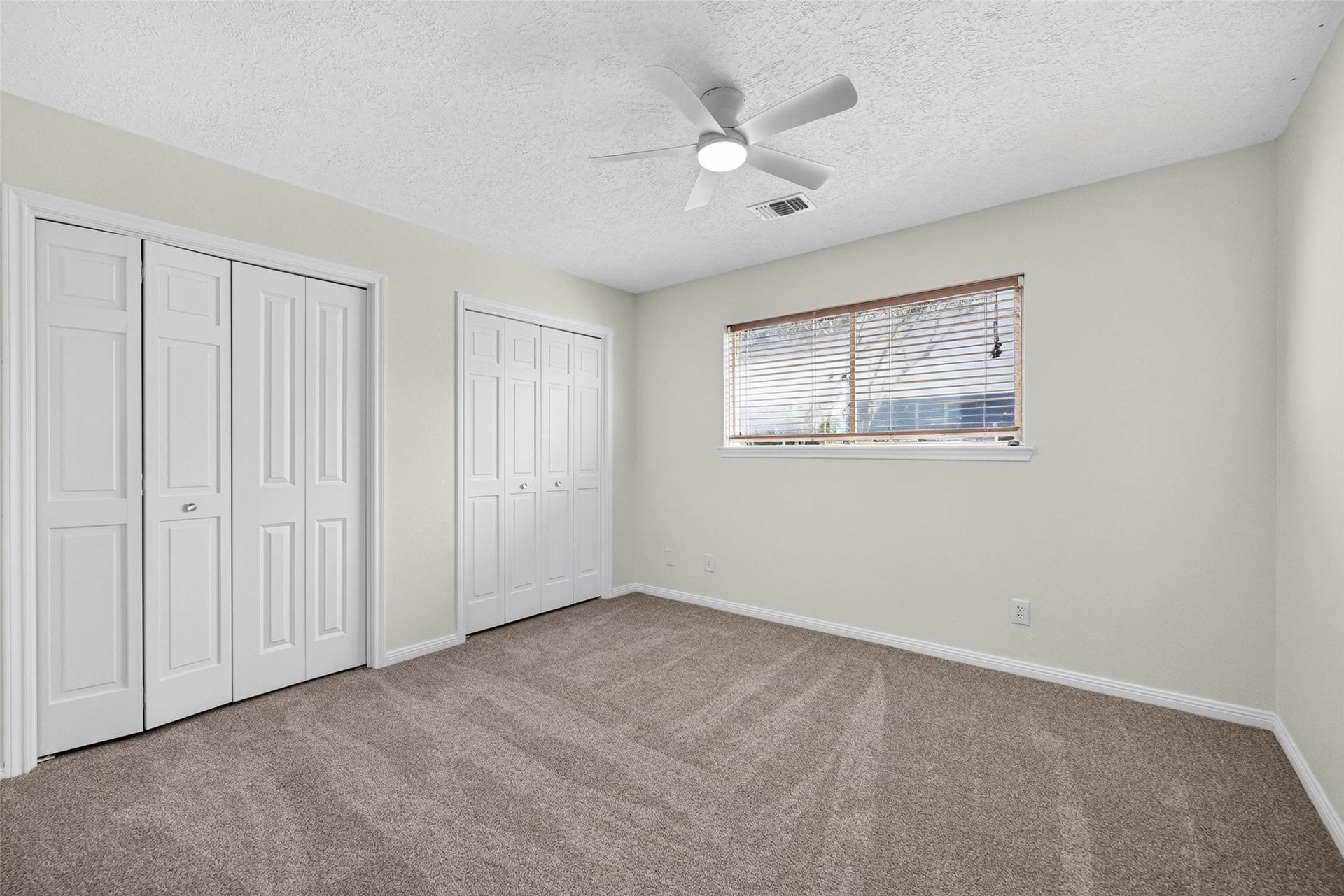 1123 Woodhorn Drive, Houston, TX 77062 Carpeted bedroom with two closet door sets and a wide window with blinds, offering flexible furniture placement.