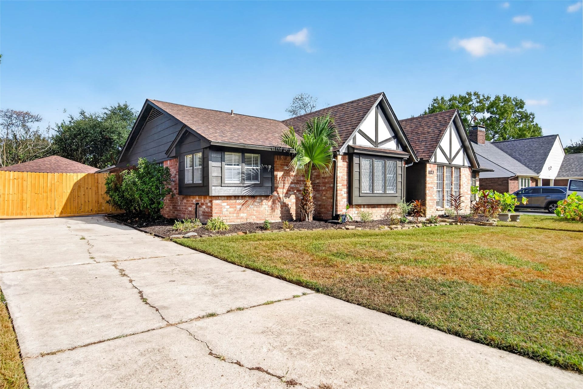 1123 Woodhorn Drive, Houston, TX 77062 Angled front view from the concrete driveway, showing the brick and dark siding exterior, brown shingle roof, wooden side fence, and landscaped bed with stone edging.