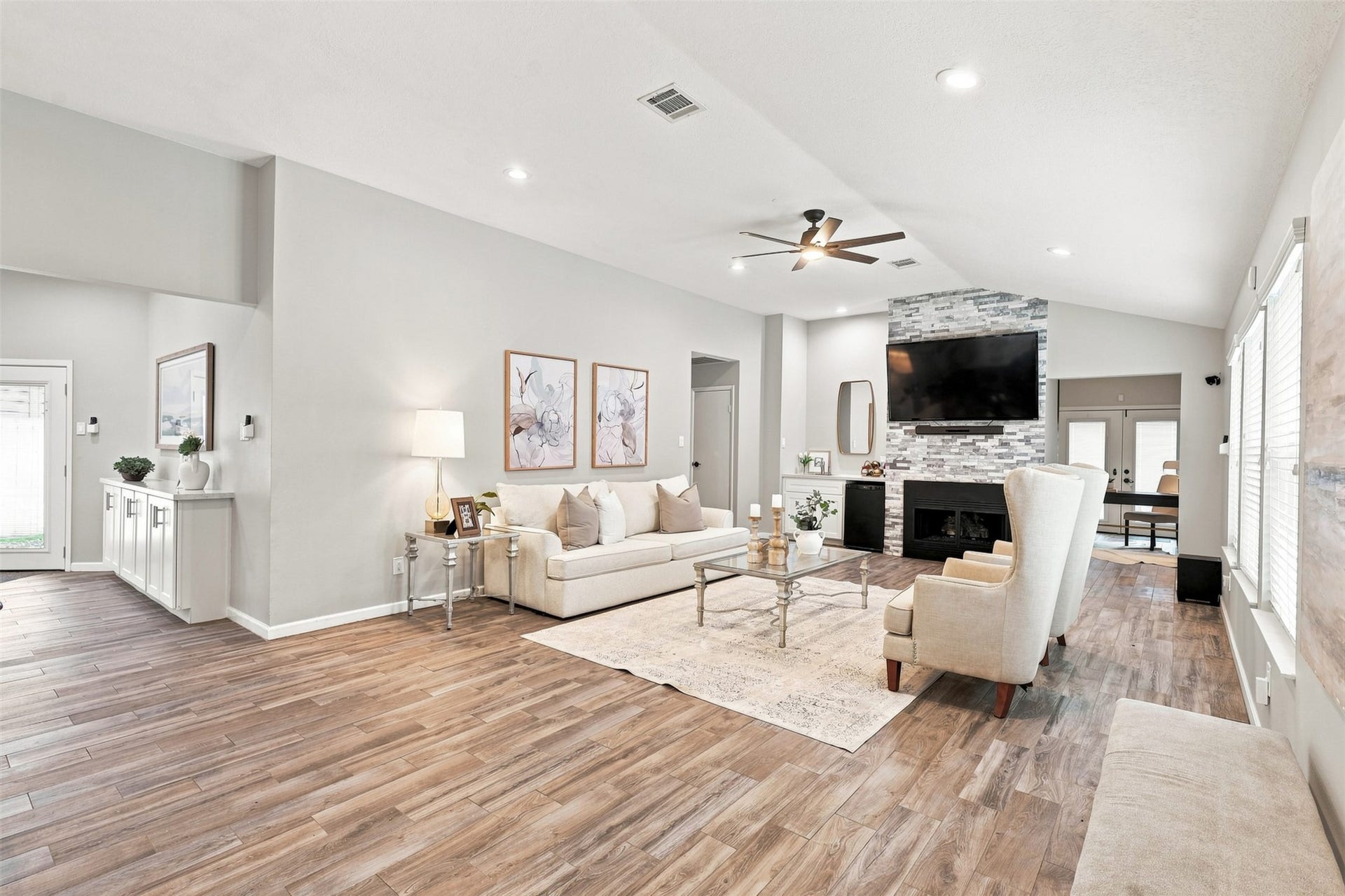 Expansive living area features vaulted ceilings, a striking floor-to-ceiling fireplace, wood-look flooring, and abundance of natural light.
