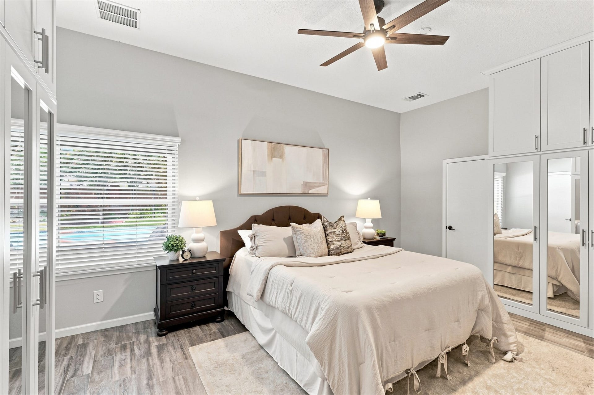 Another view of the primary bedroom highlights abundant built-in storage, mirrored cabinetry, high ceiling, and a large window overlooking the backyard and pool.