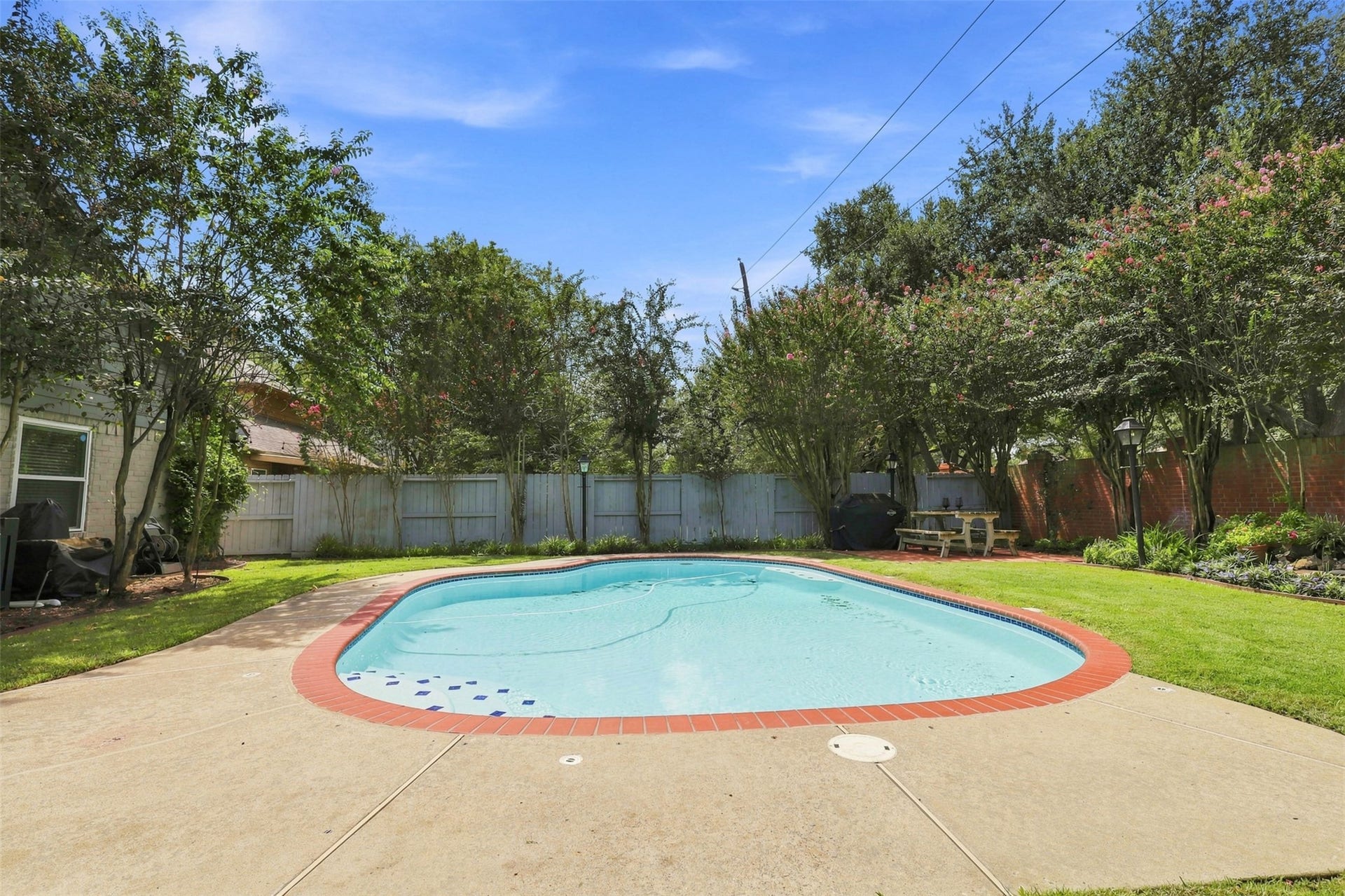 Sparkling in-ground pool anchors the private backyard, surrounded by mature trees, green lawn, and established landscaping for a peaceful outdoor retreat.