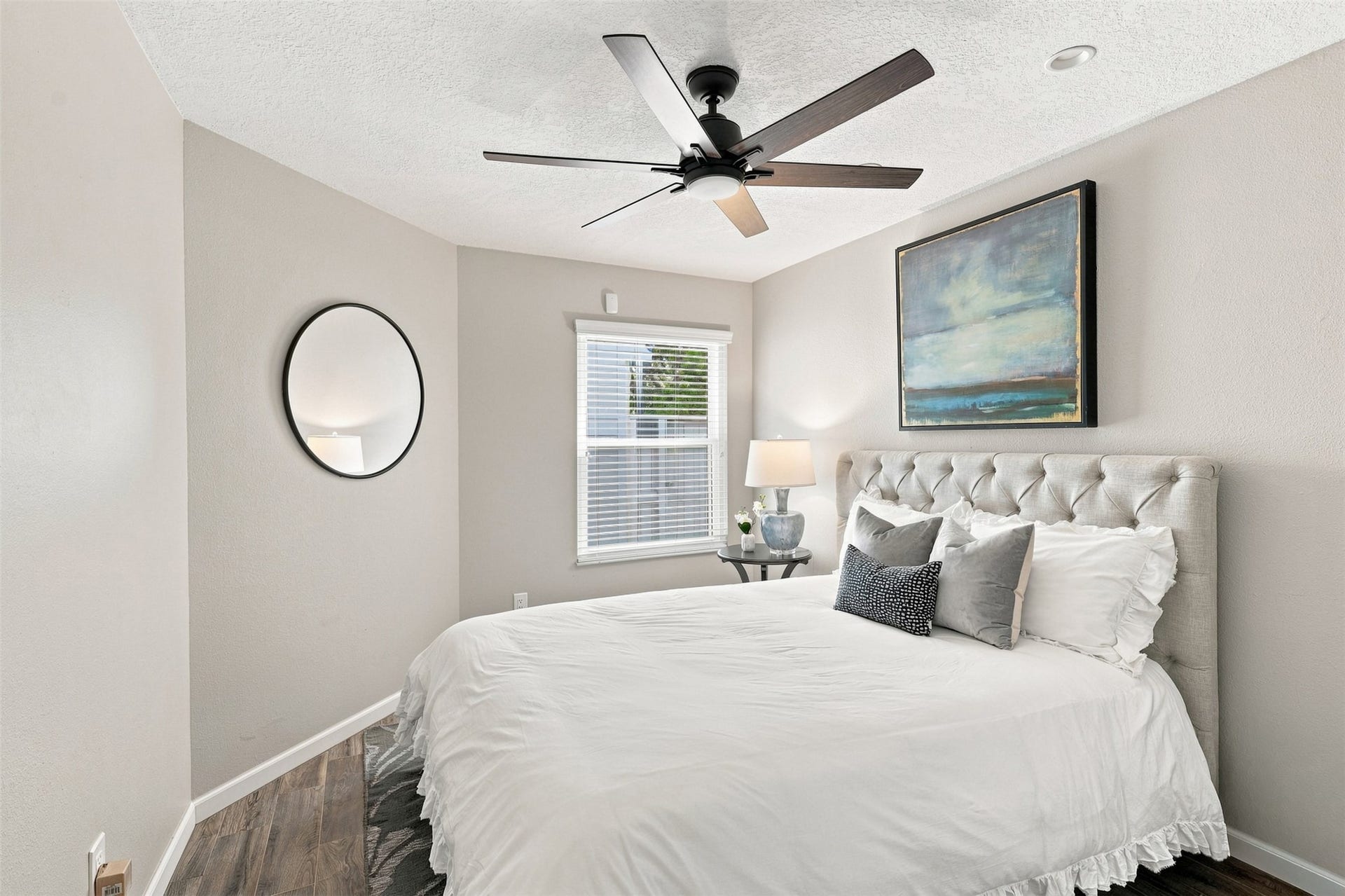 Comfortable secondary bedroom features wood-look tile flooring, a ceiling fan, neutral finishes, and natural light from a large window.