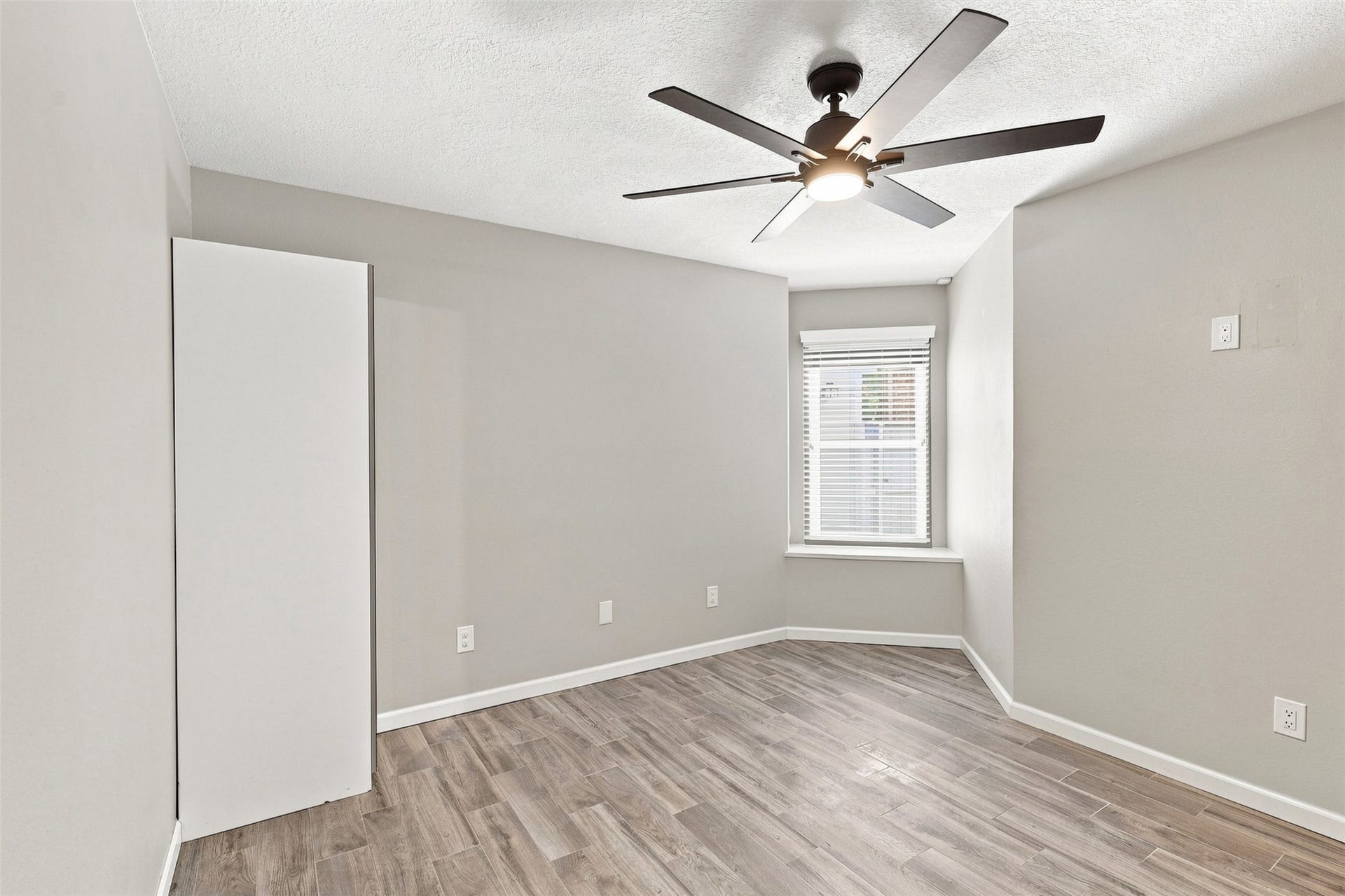 Additional secondary bedroom offers wood-look flooring, neutral finishes, a ceiling fan, and a window providing natural light.