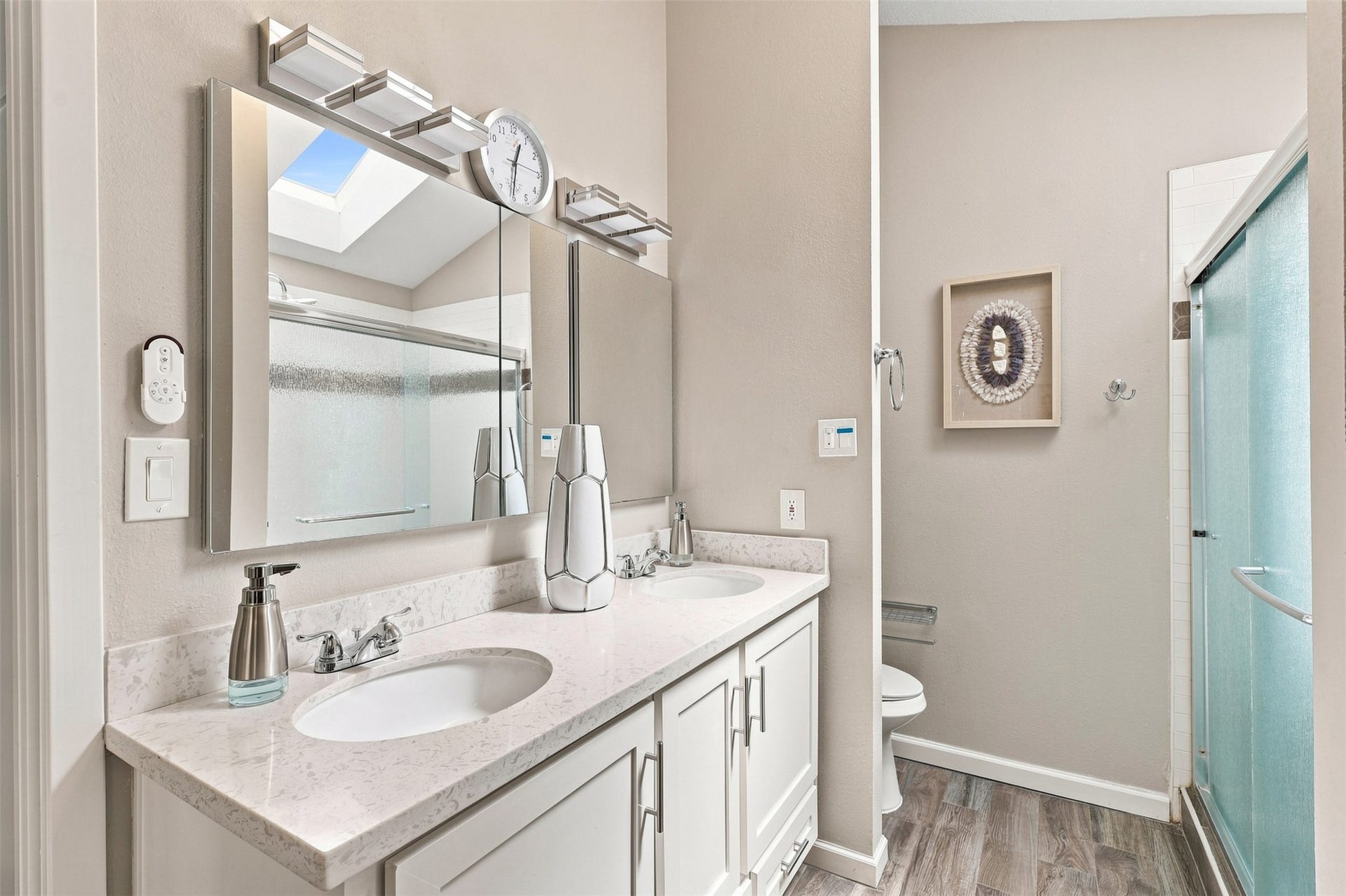 Primary bathroom features a dual-sink vanity with generous counter space, updated lighting, and a glass-enclosed shower illuminated by a skylight above.