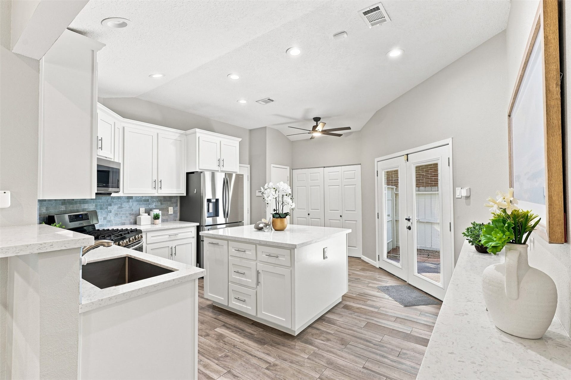 Updated kitchen features crisp white cabinetry, quartz countertops, a center island with additional storage, stainless steel appliances, and a stylish tile backsplash.
