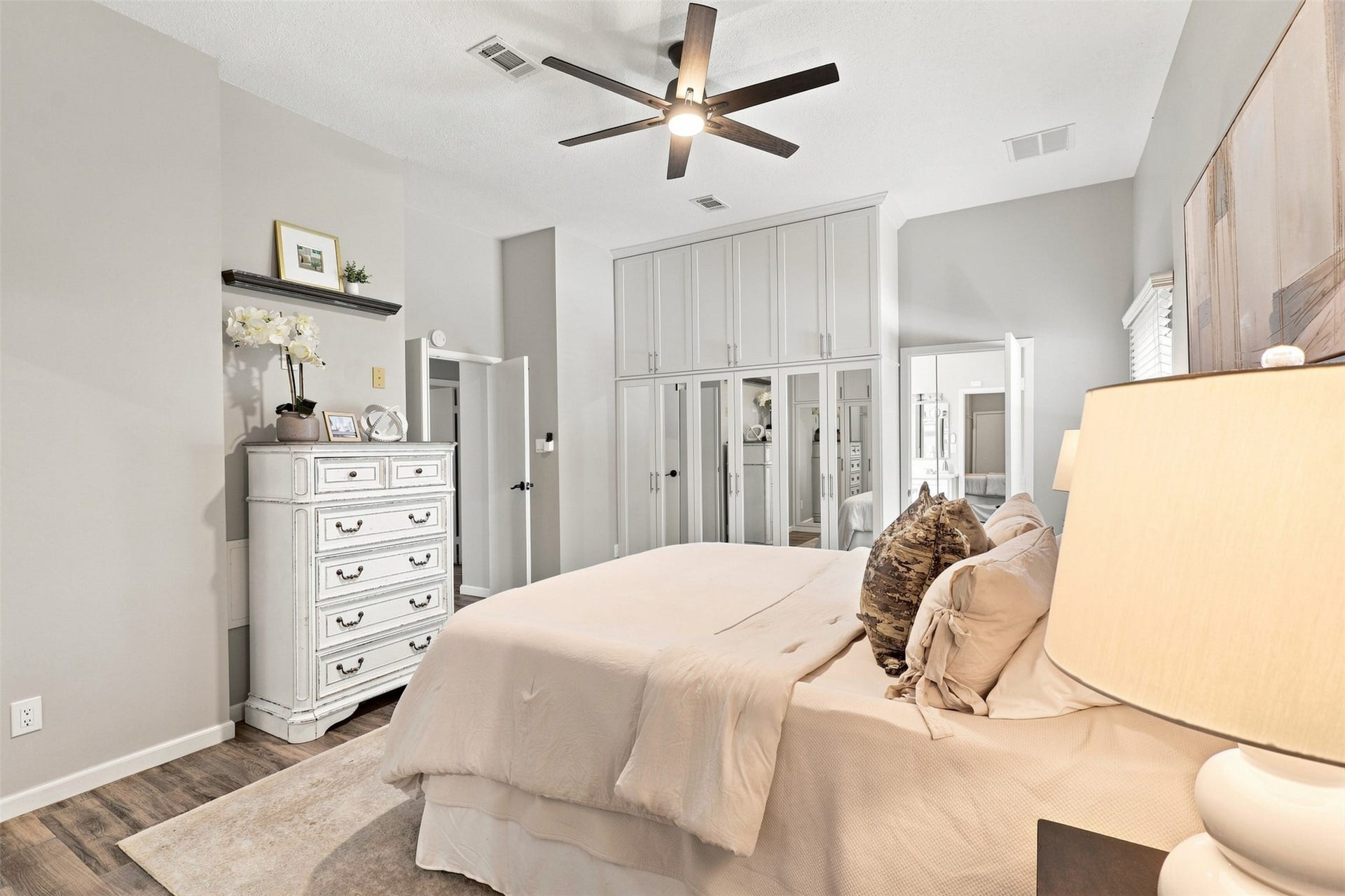 Primary bedroom features high ceilings, wood-look tile flooring, ceiling fan, and extensive built-in cabinetry providing abundant storage.