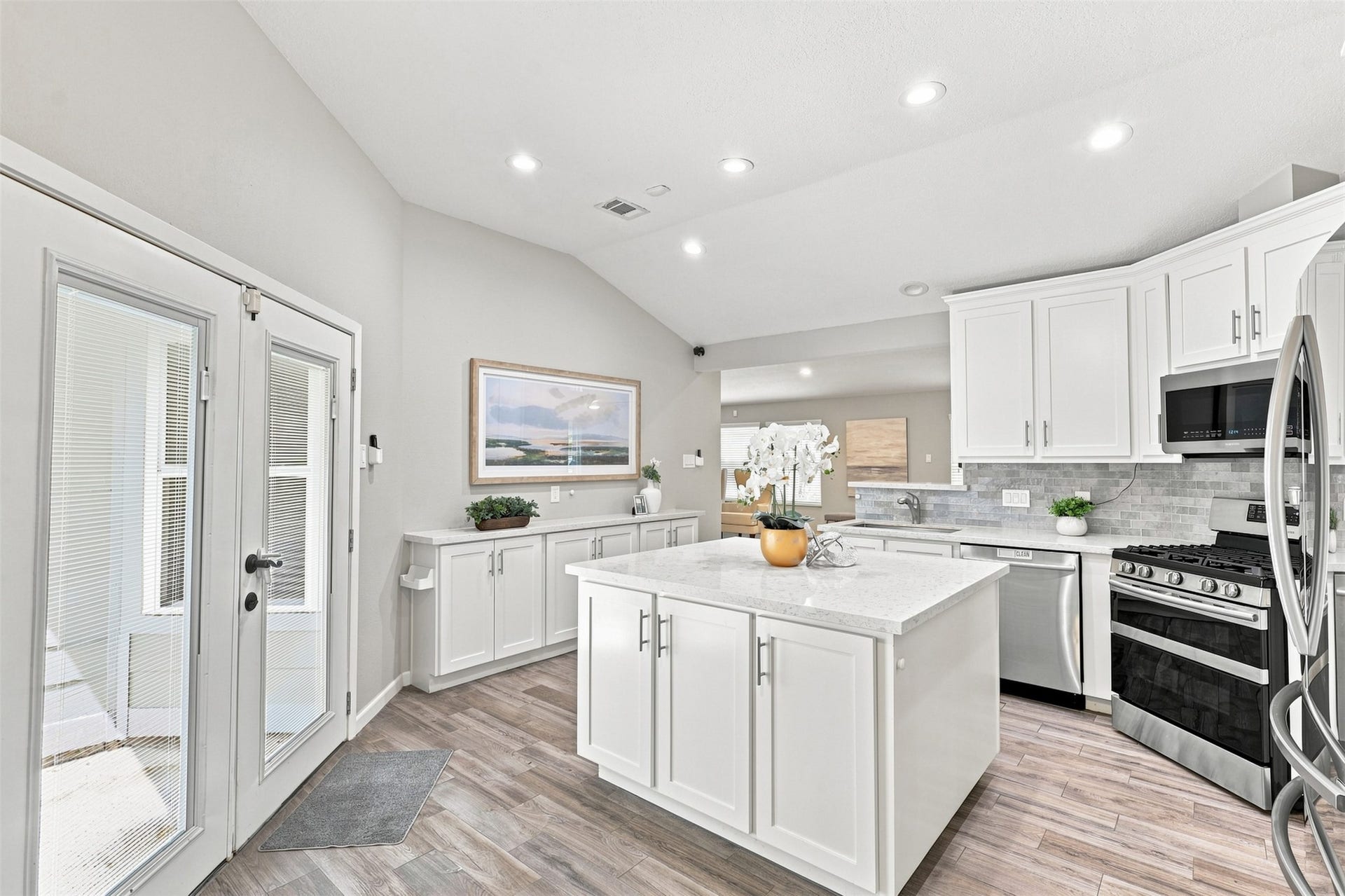 Another view of the updated kitchen highlights the large center island, abundant cabinetry and counter space, stainless steel appliances, and French doors providing easy outdoor access.