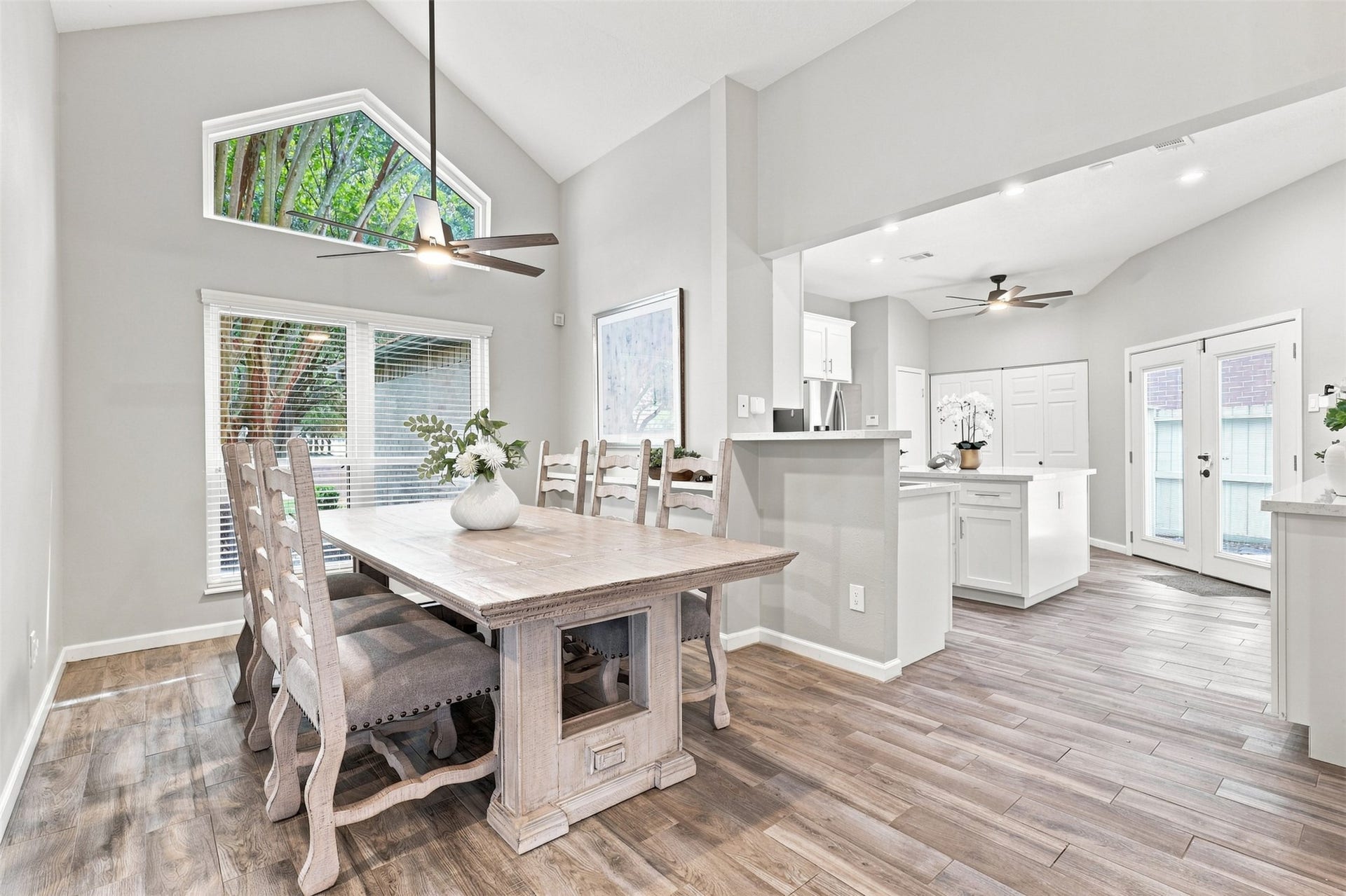 Dining area features a soaring vaulted ceiling, distinctive architectural window, and large windows overlooking the mature trees, with an open connection to the kitchen.