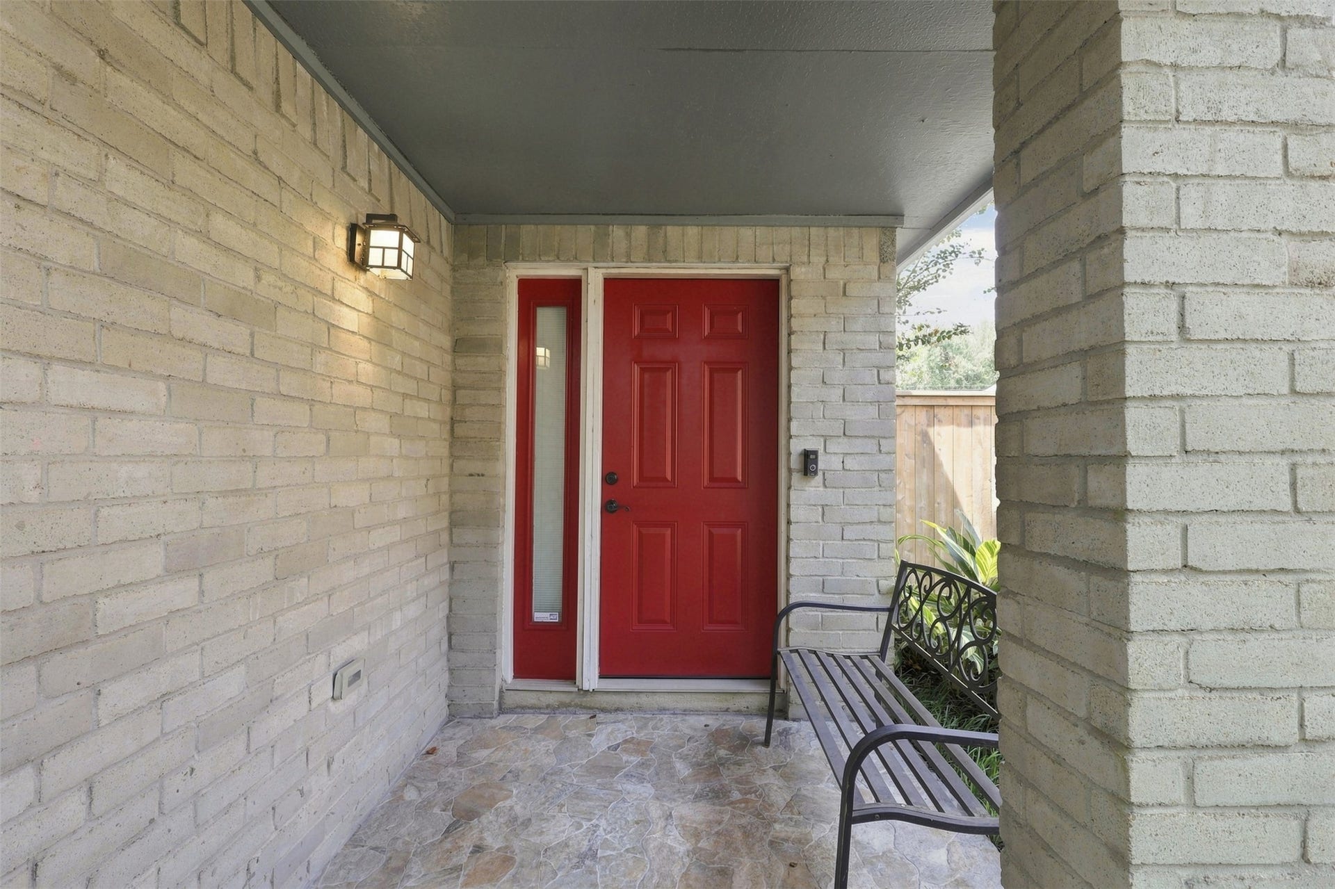 Welcoming covered front entry featuring a bold red front door with sidelight, brick surround, and tiled porch area.