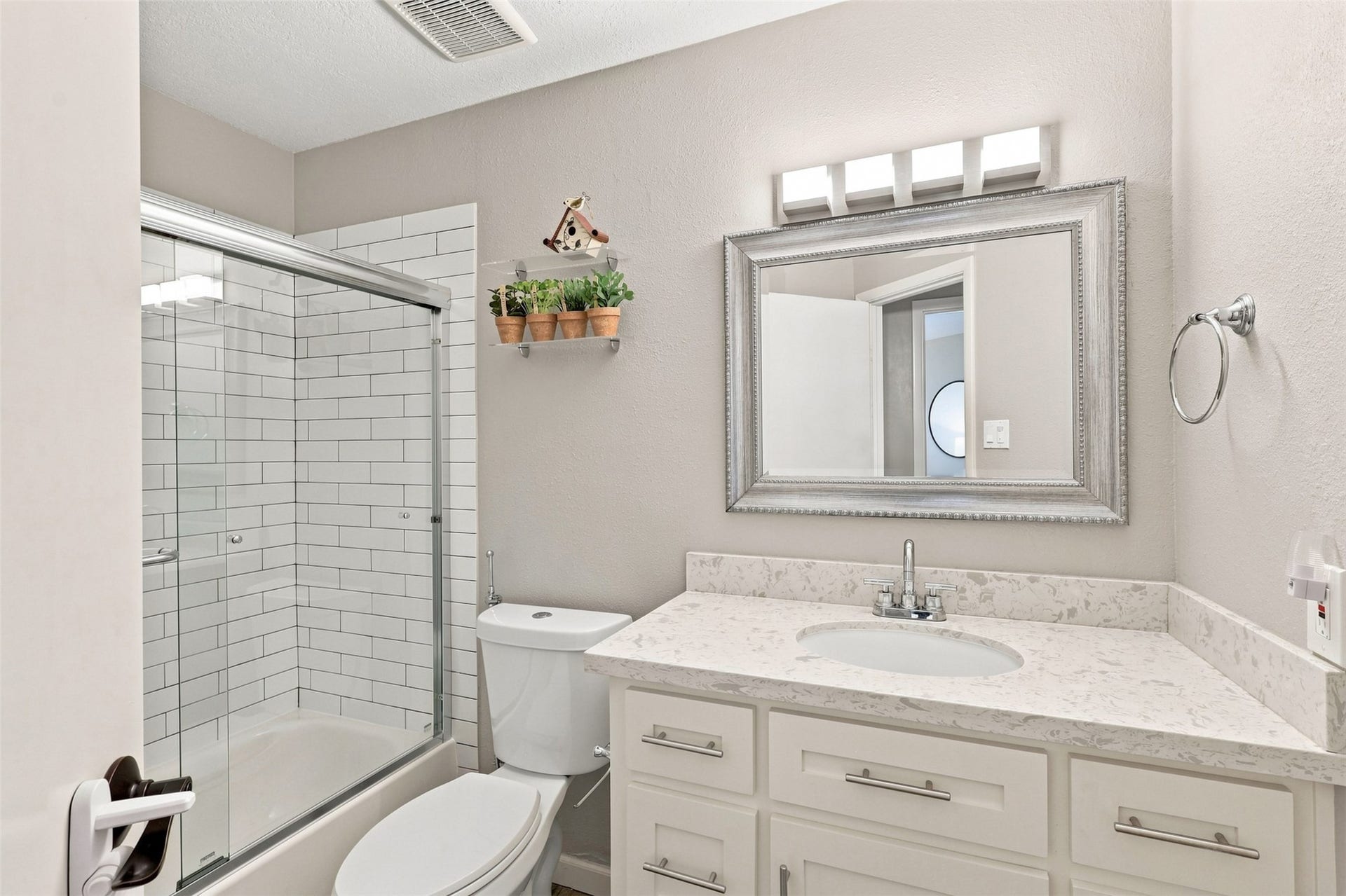 Updated secondary bathroom features a quartz-topped vanity, modern fixtures, and a tub/shower combination with classic subway tile surround and glass enclosure.