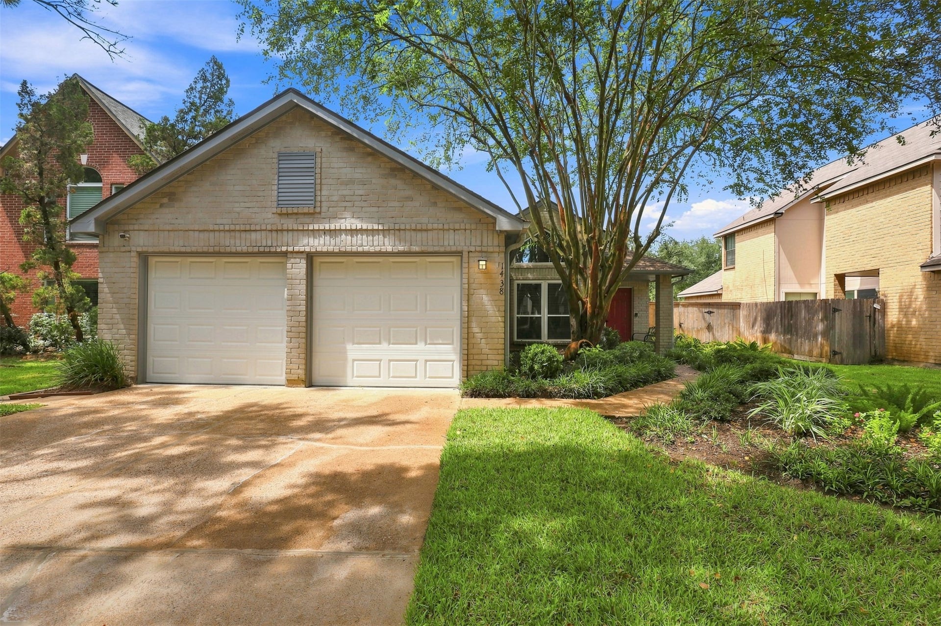 Charming single-story home with a two-car garage, mature shade trees, well-maintained landscaping, welcoming red front door, and an extended driveway.