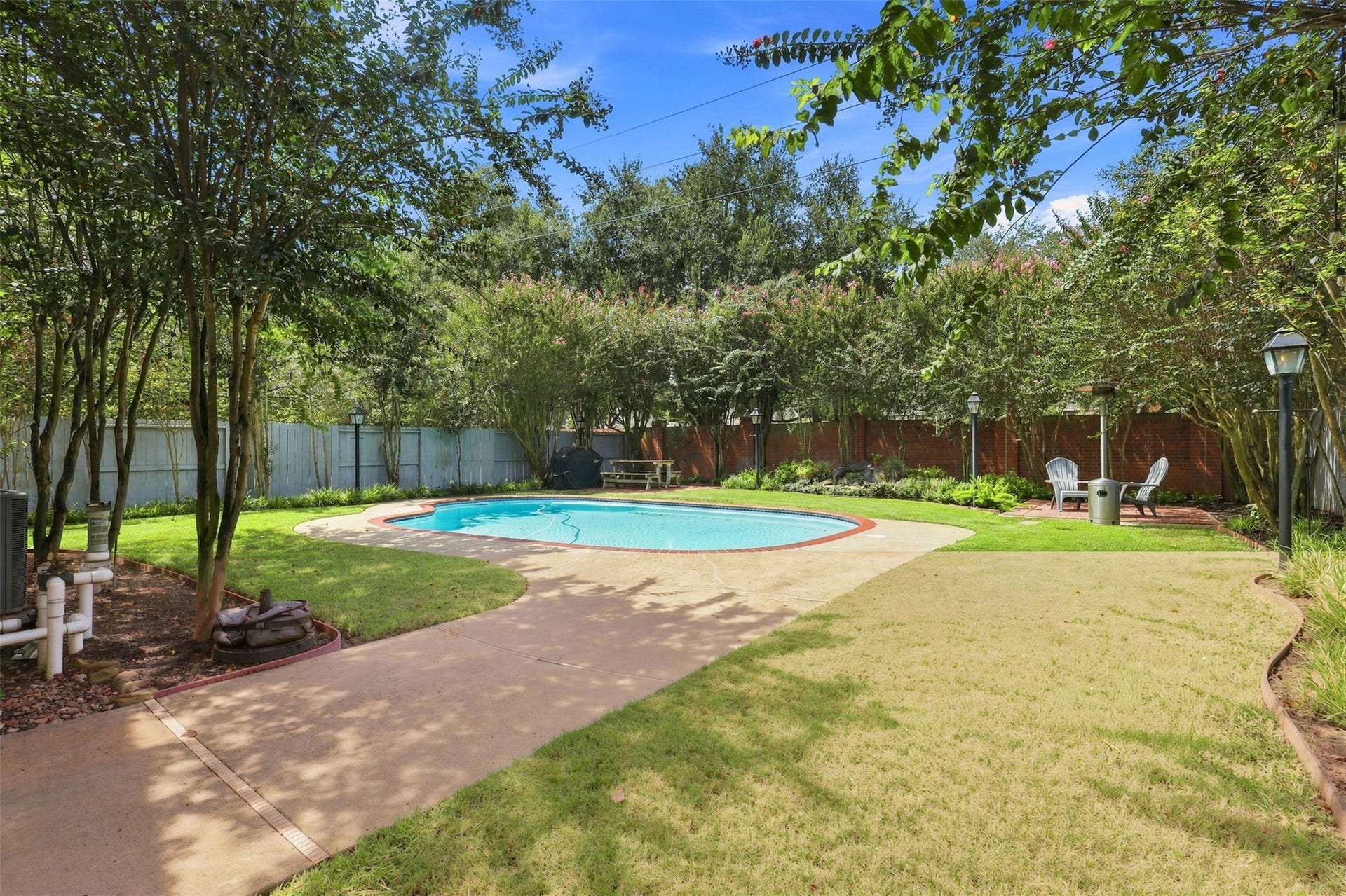 Discover a serene backyard oasis featuring a sparkling pool surrounded by lush greenery and ample patio space, perfect for relaxation and outdoor entertaining.